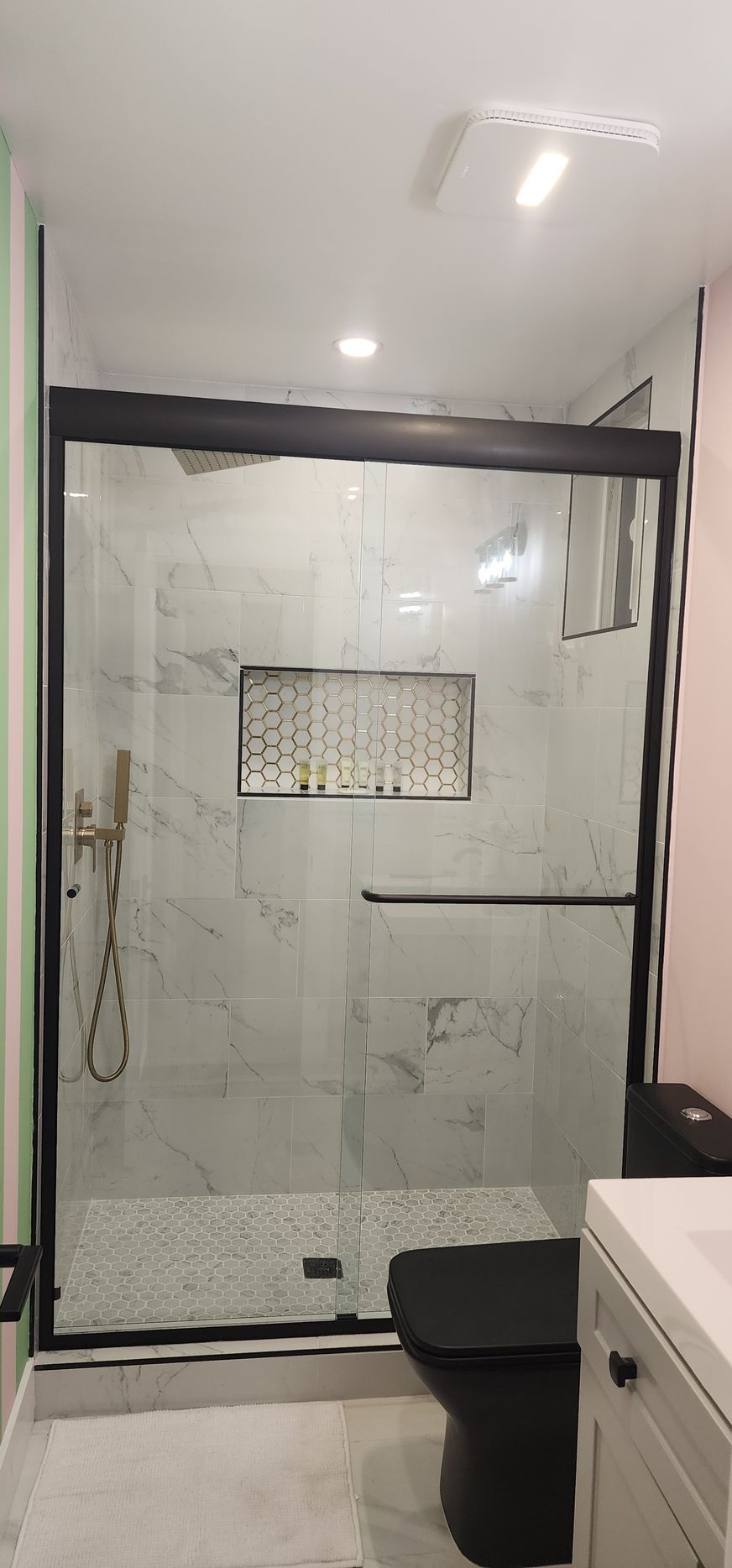 A modern bathroom featuring a glass-enclosed shower with a black frame, marble-patterned walls, and a black toilet.