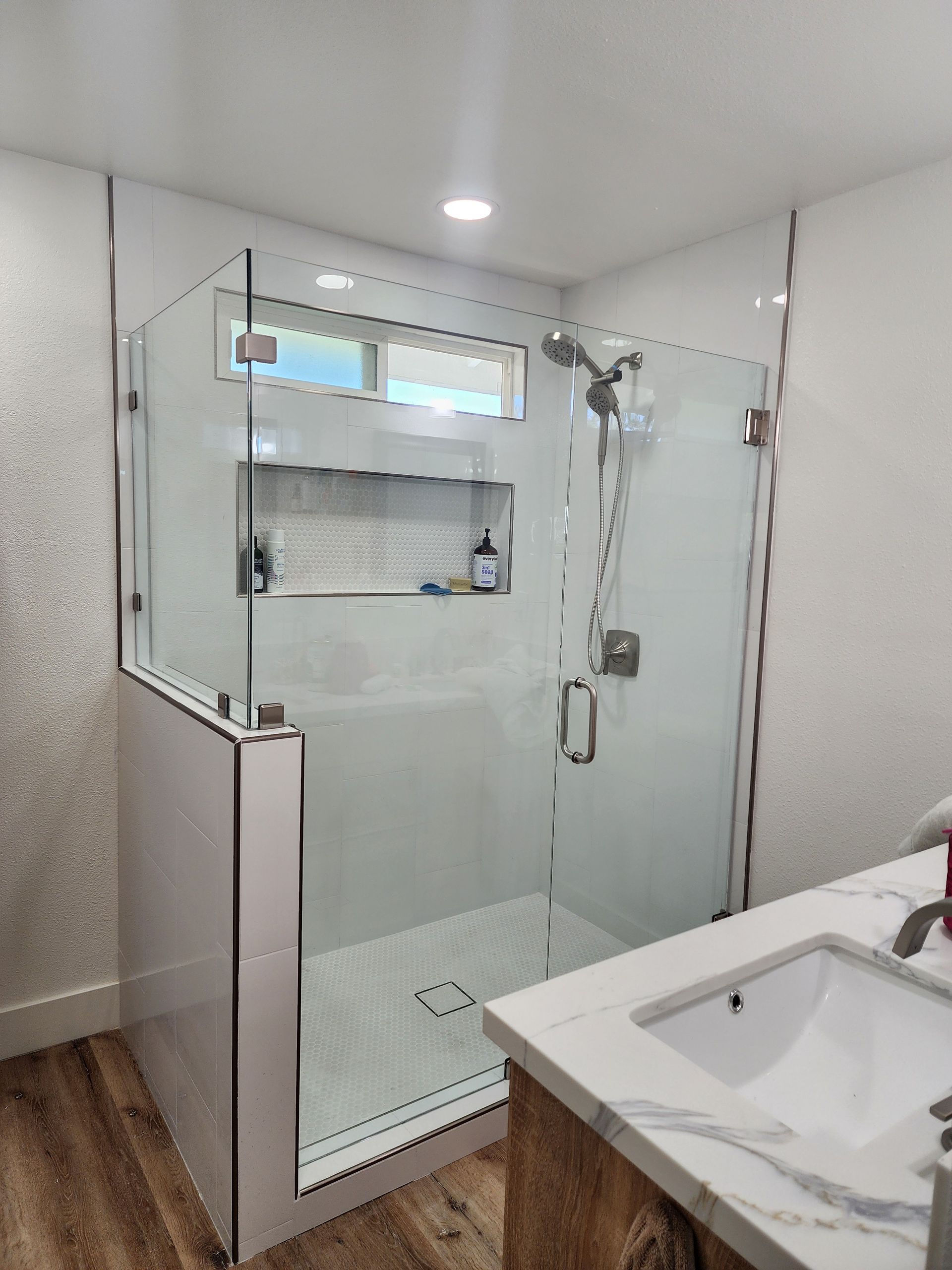 A modern bathroom featuring a glass-enclosed shower with white tiled walls, a built-in niche, and a white marble vanity.