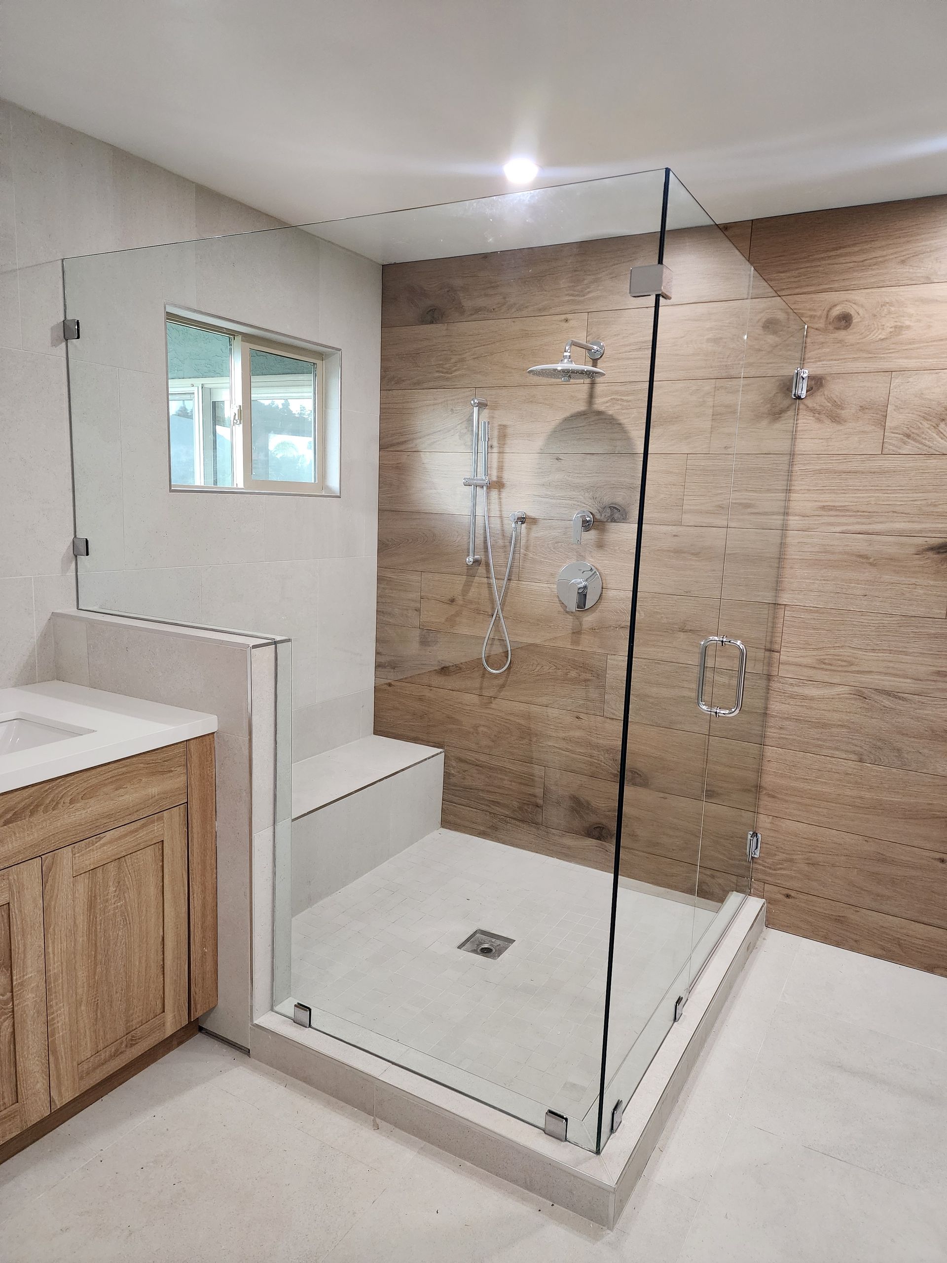 Modern bathroom shower with glass enclosure, white tiled base, a built-in bench, and wood-look wall tiles.