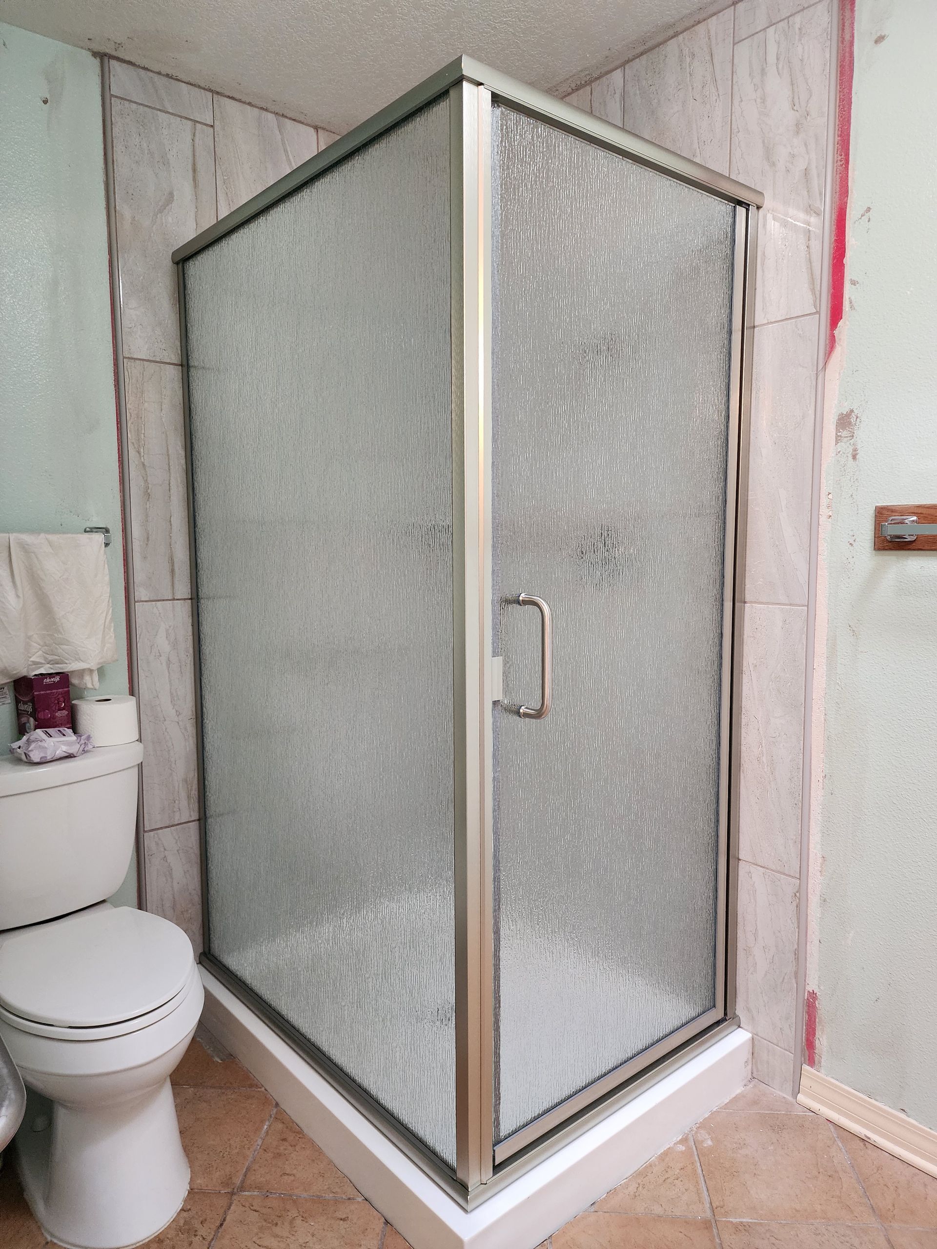 A white toilet sits next to a square shower stall with silver frames and frosted, textured glass doors in a bathroom.