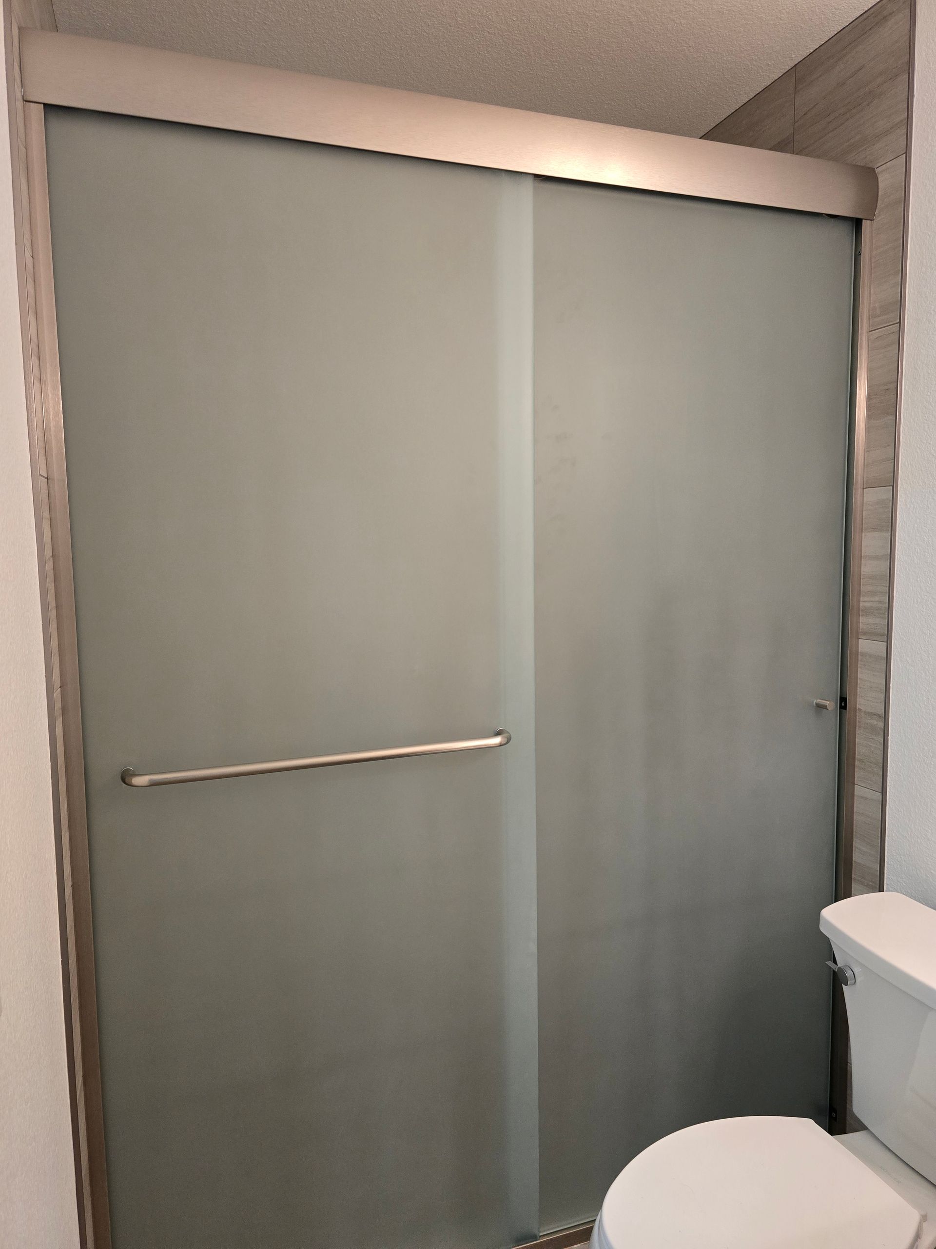 Frosted glass sliding shower doors with a silver frame and handle, installed in a bathroom next to a white toilet.
