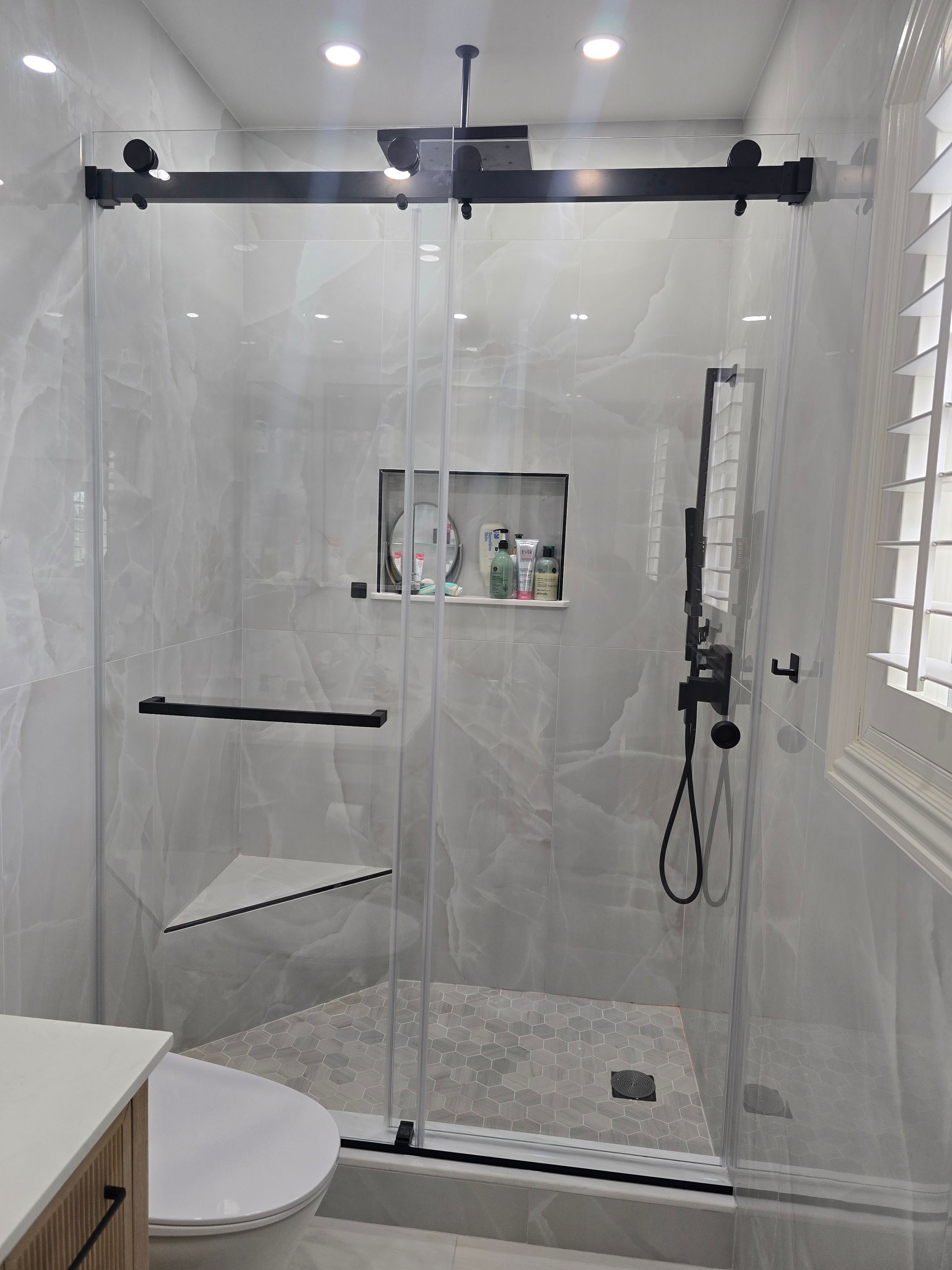 Modern walk-in shower with a black sliding glass door, white tiled walls, a built-in shelf, and a corner seat.