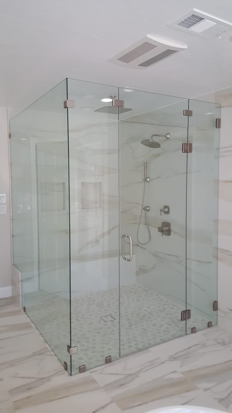 A glass-enclosed walk-in shower with stone tile floors and walls, featuring brushed metal fixtures and hardware.