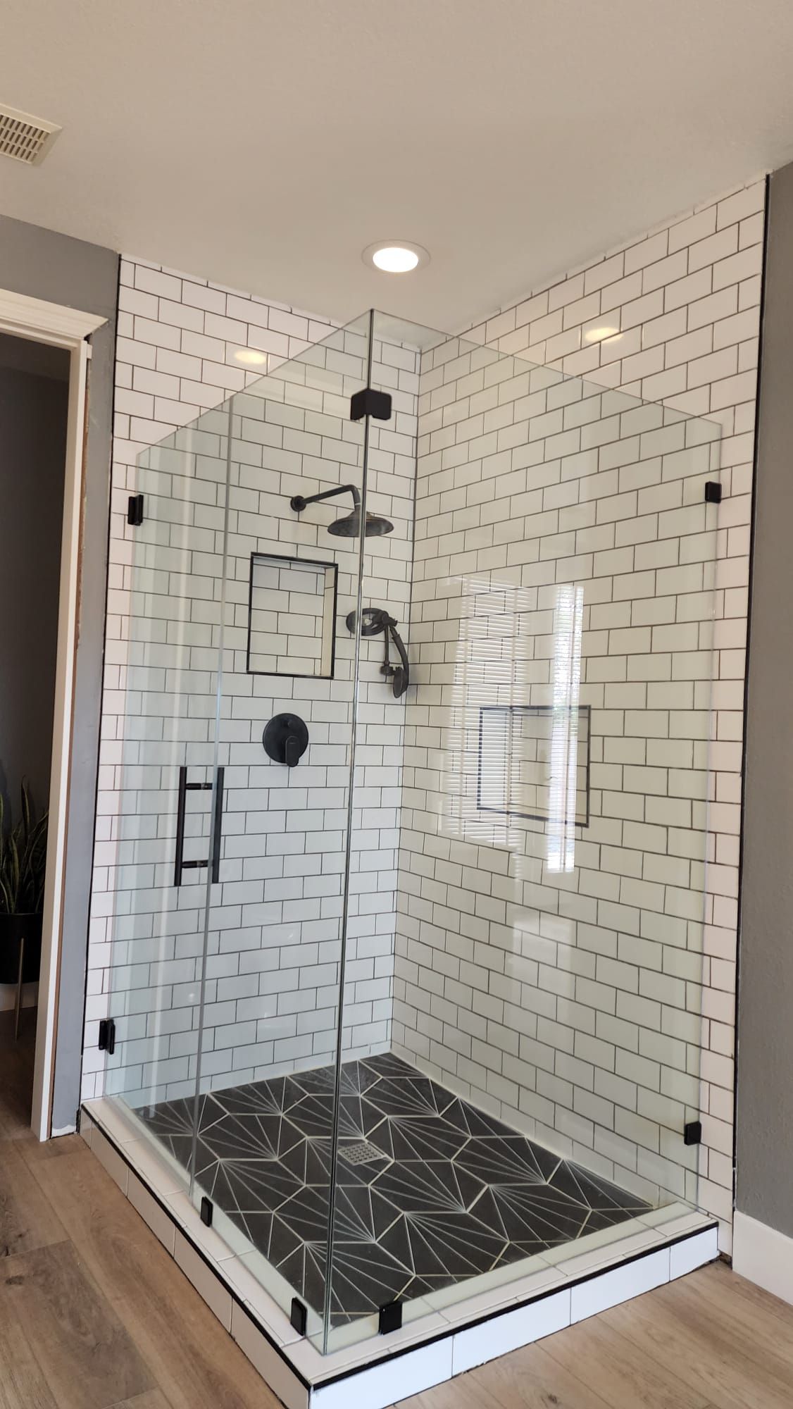 A modern walk-in shower with white subway tile walls, black hexagonal floor tiles, and a clear glass enclosure.