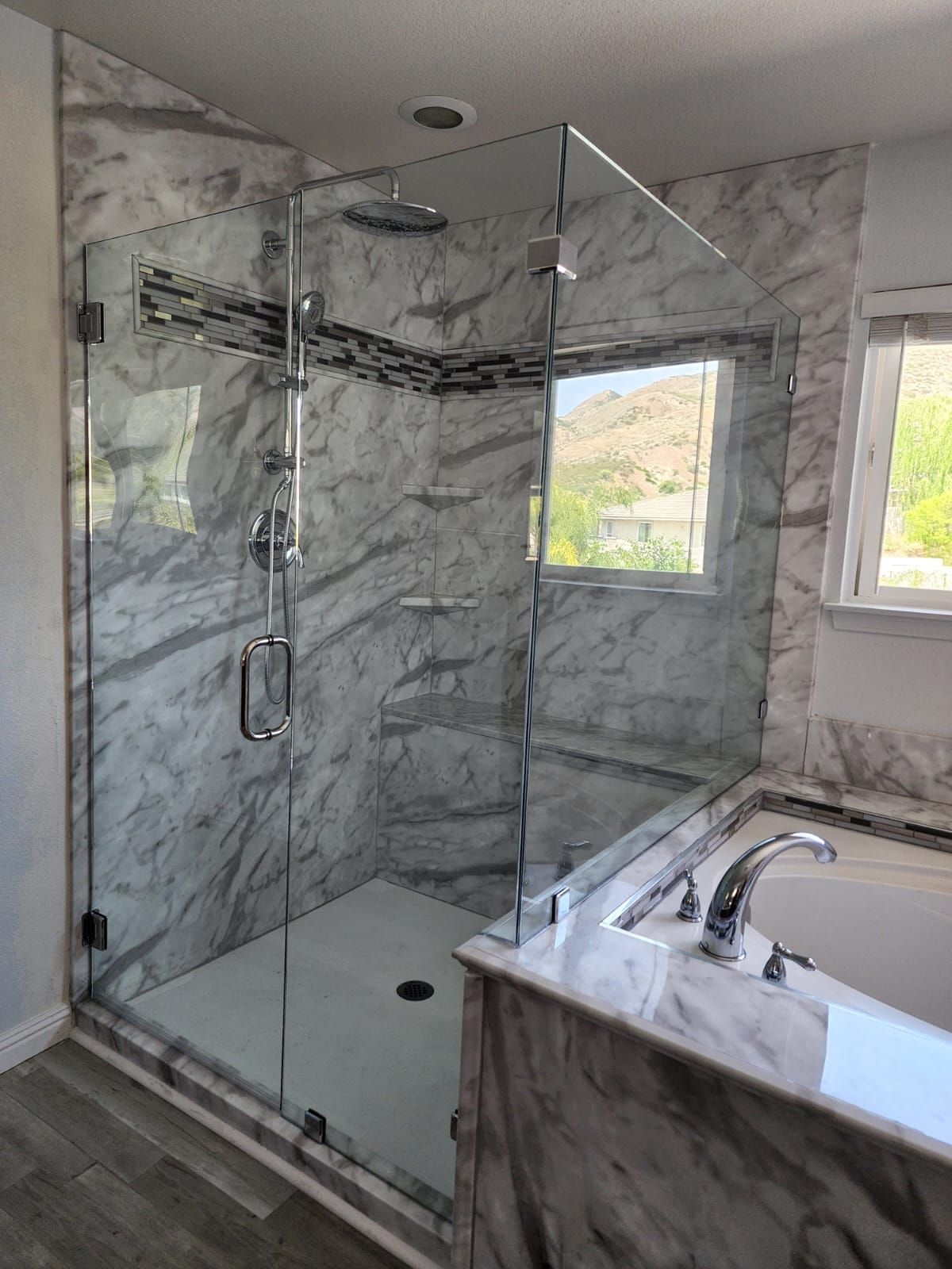 A marble-tiled walk-in shower with a glass enclosure and rain showerhead, next to a matching marble-surround bathtub.