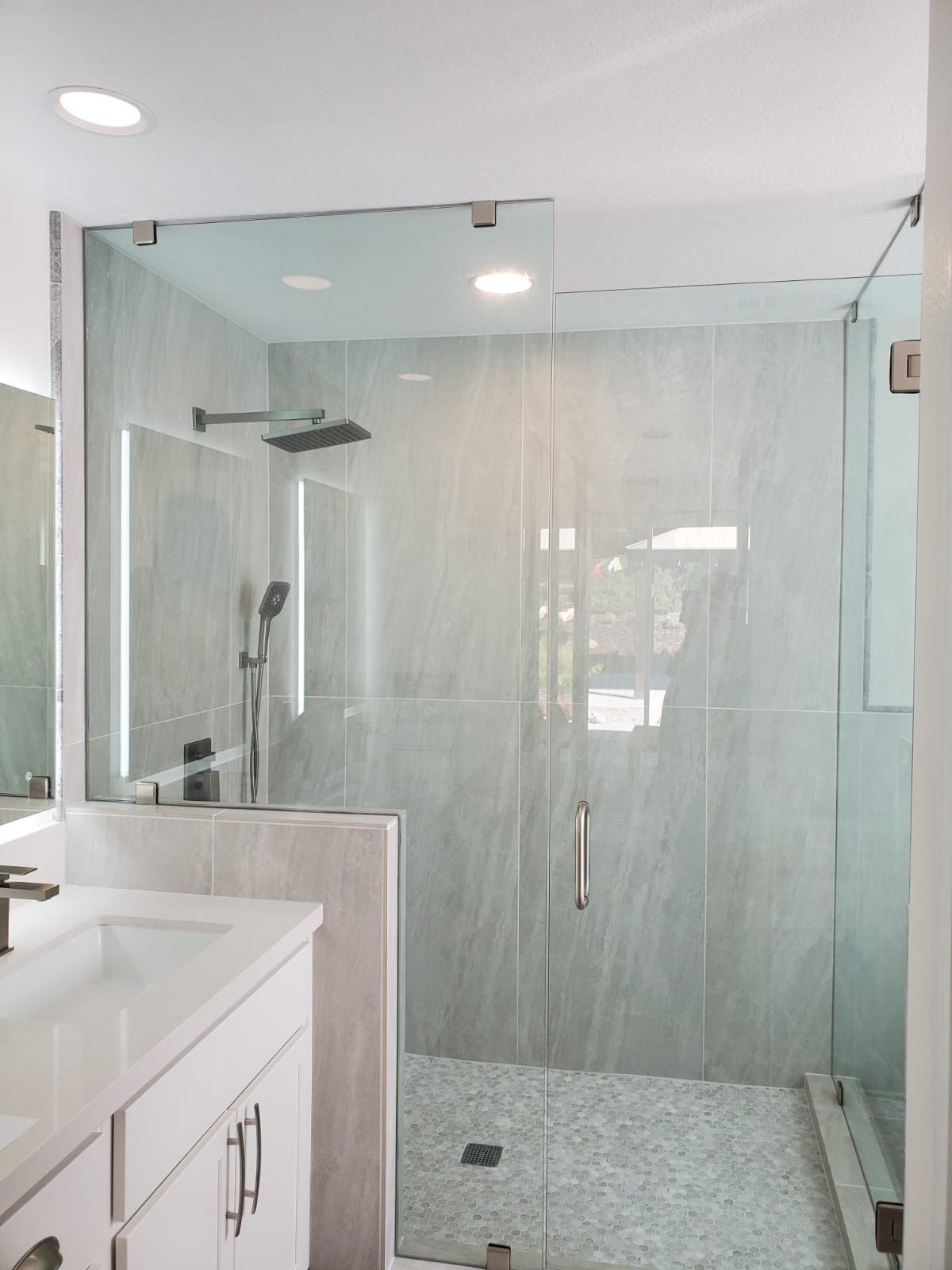 A bathroom with a white vanity and a glass-enclosed shower featuring light gray marble-look tile walls and a pebble floor.
