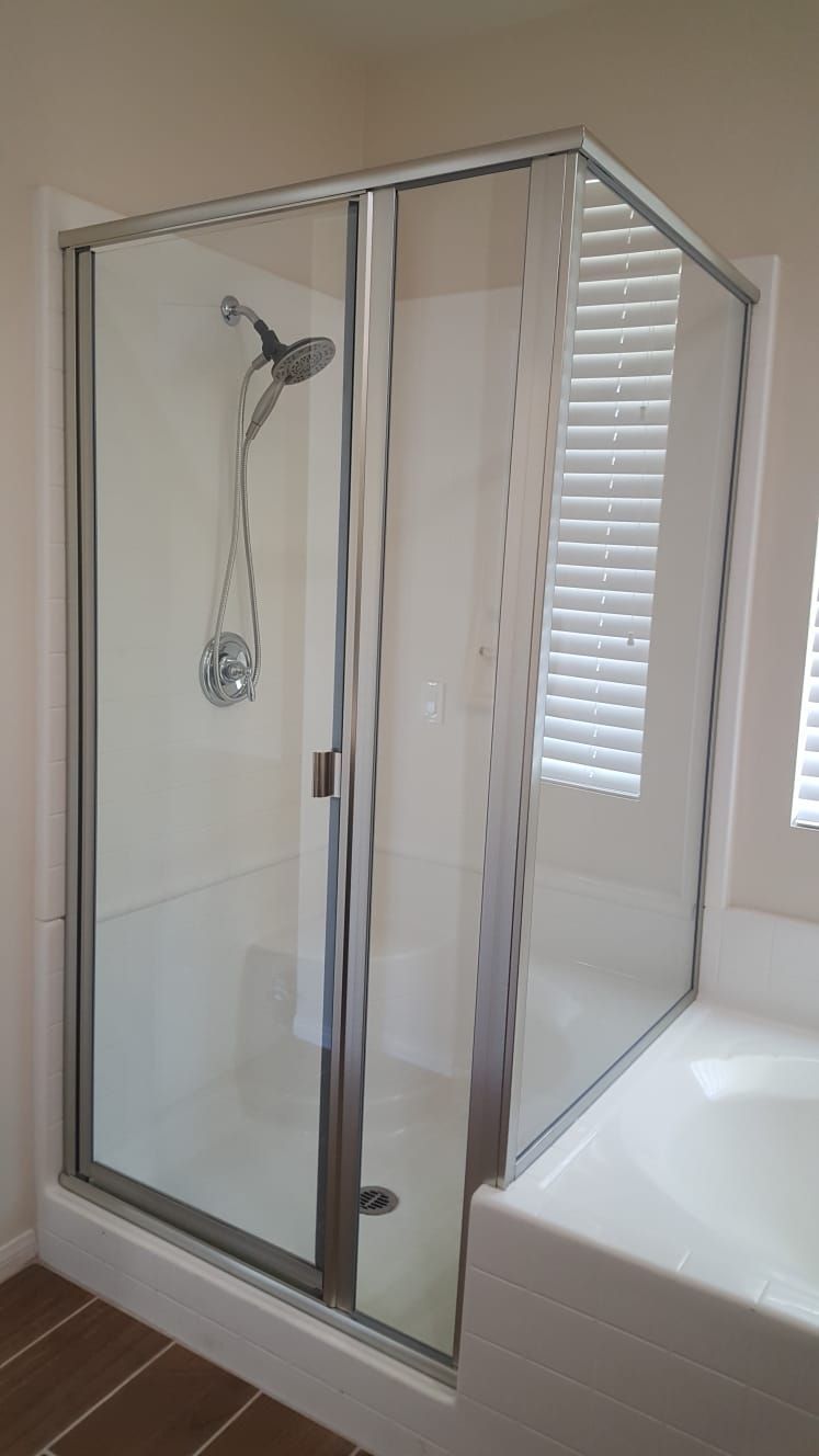 A corner shower unit with glass doors, a silver frame, and a shower head inside, next to a white bathtub.