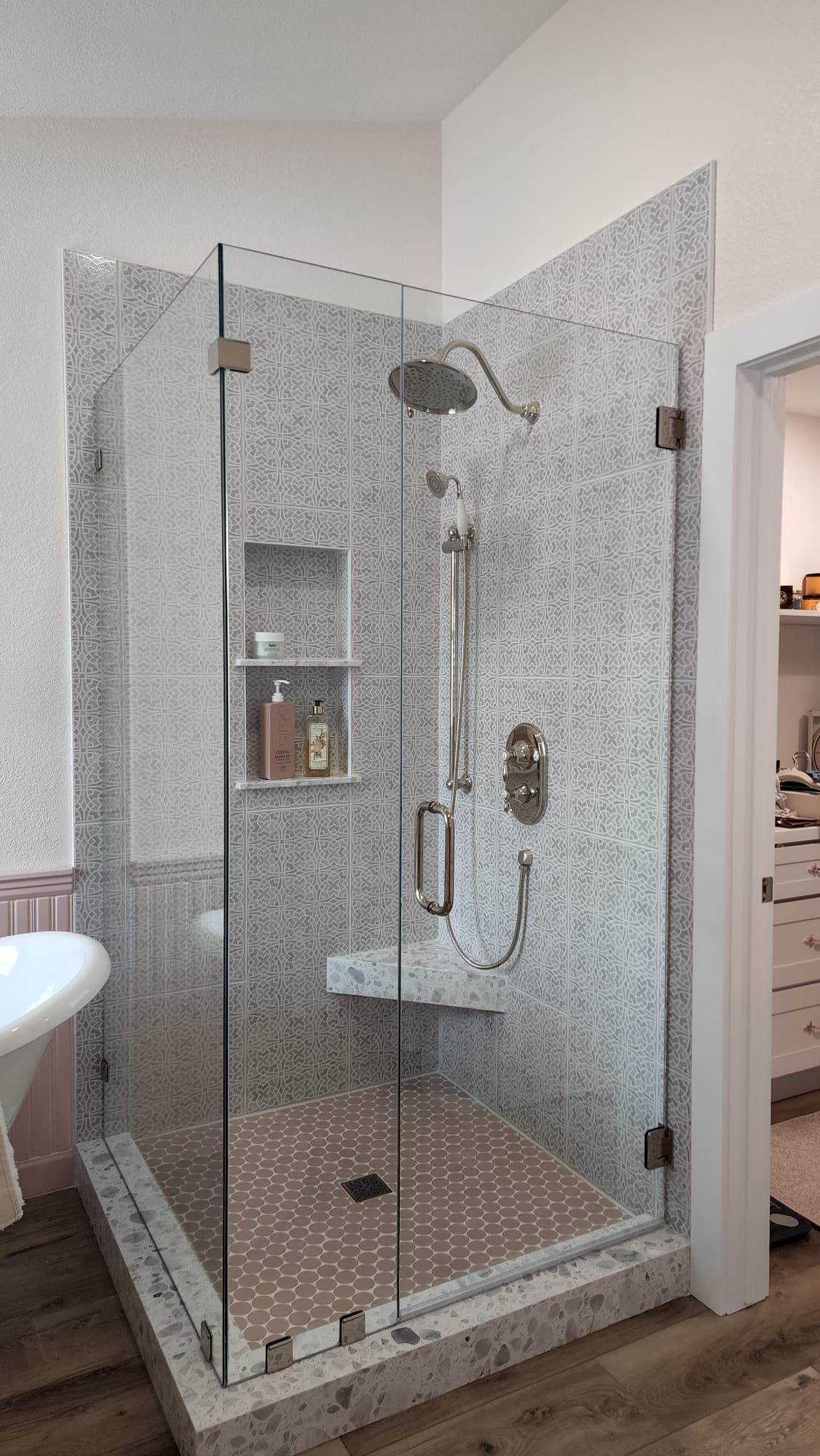 A modern glass-enclosed shower with grey speckled tile, a built-in corner bench, a niche for toiletries, and metal fixtures.