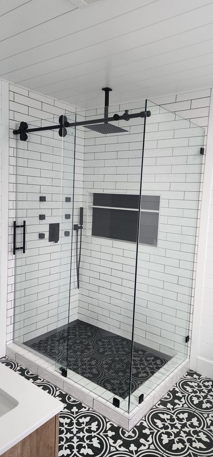 A modern glass shower enclosure with matte black hardware, white subway tile walls, and a dark stone floor.