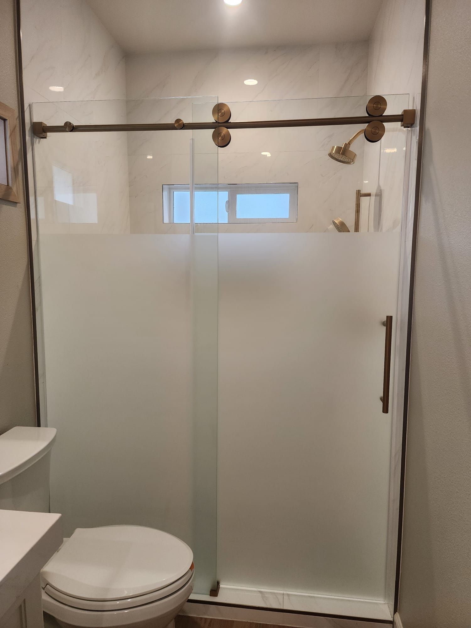 A glass sliding shower door with gold hardware and frosted privacy glass installed in a modern bathroom.