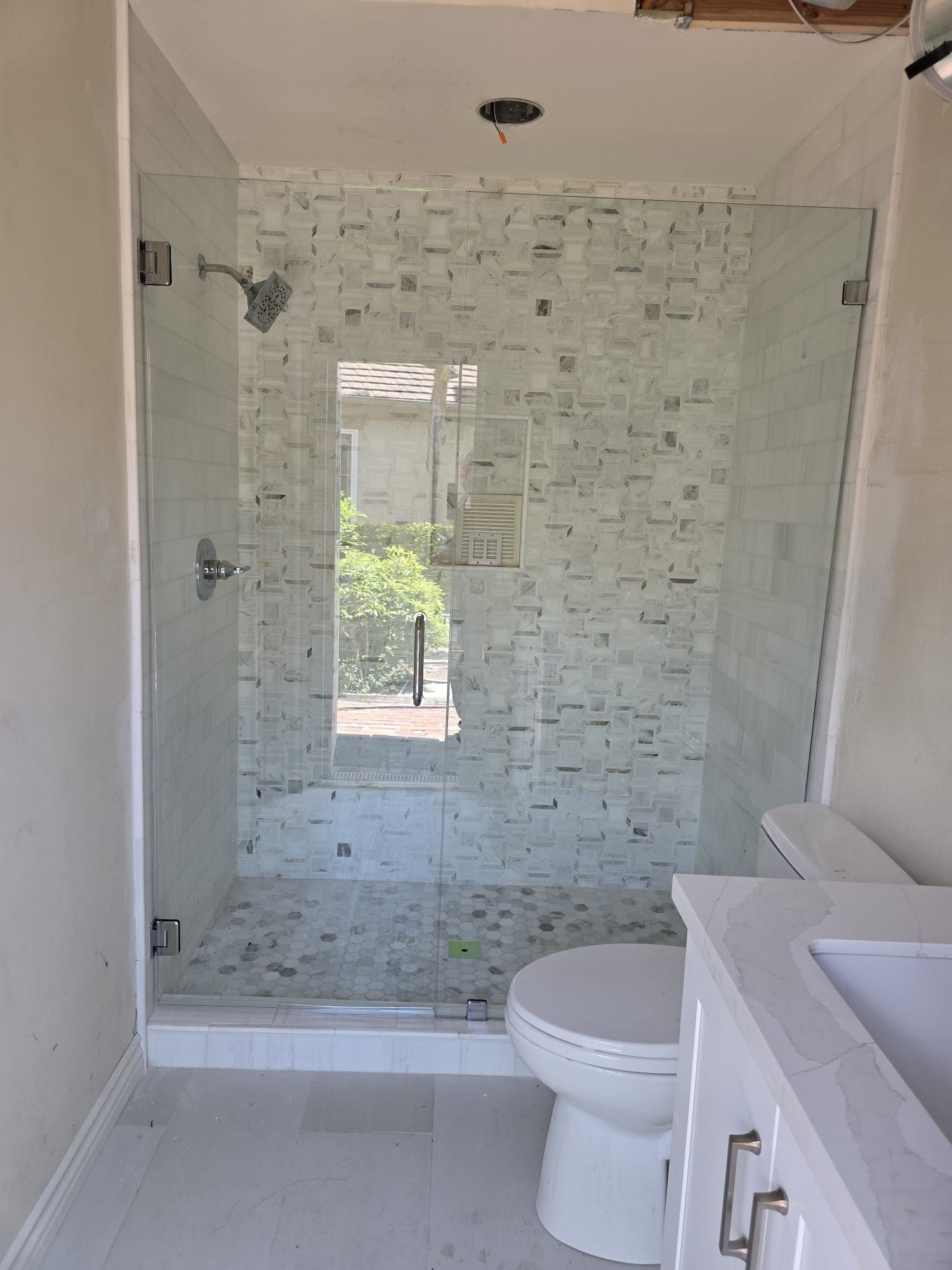 A bathroom with a tiled walk-in shower enclosed in glass, a white toilet, and a white vanity.