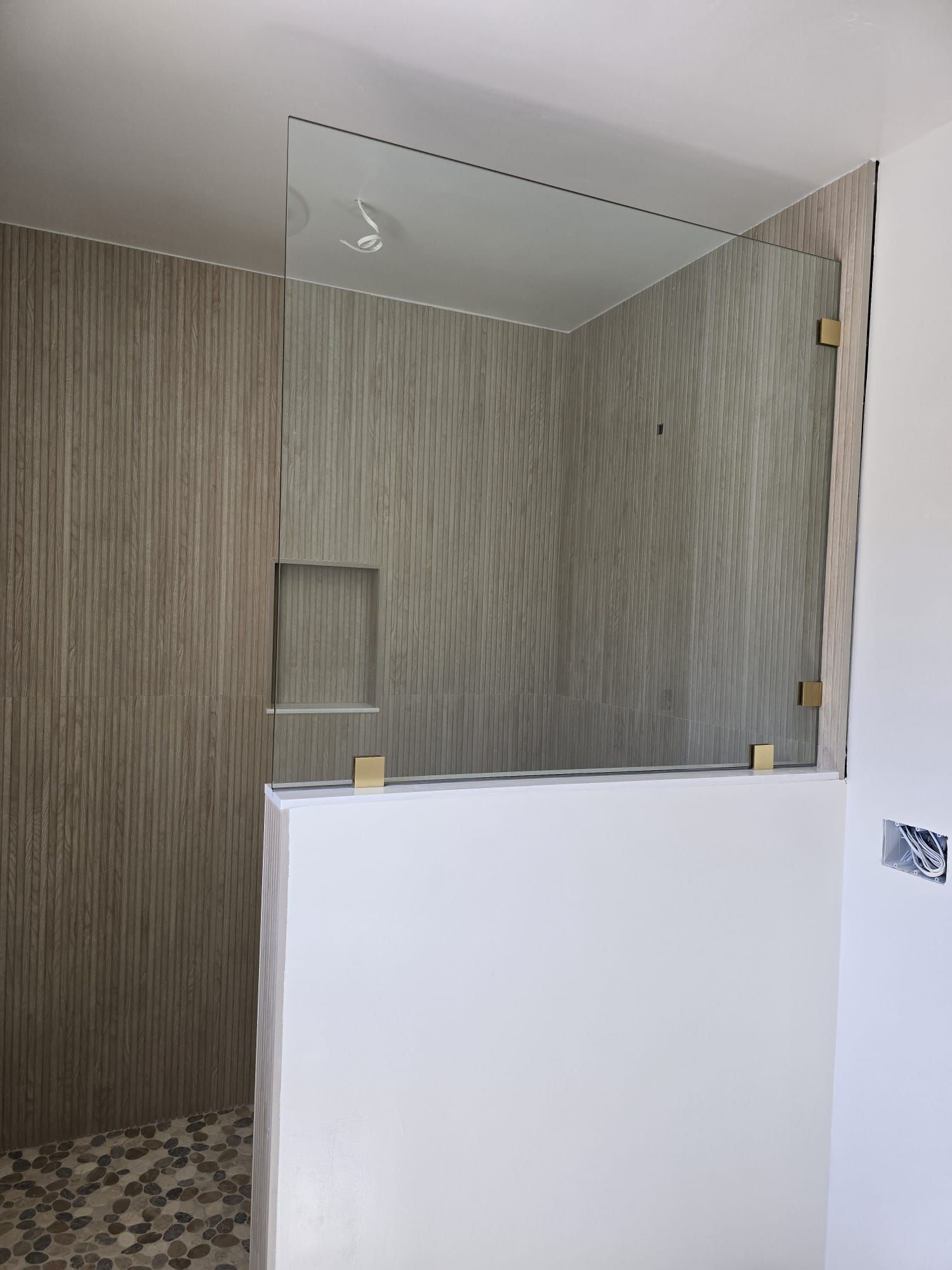 A walk-in shower with vertical wood-patterned tile, a small recessed niche, and a glass panel atop a white half-wall.