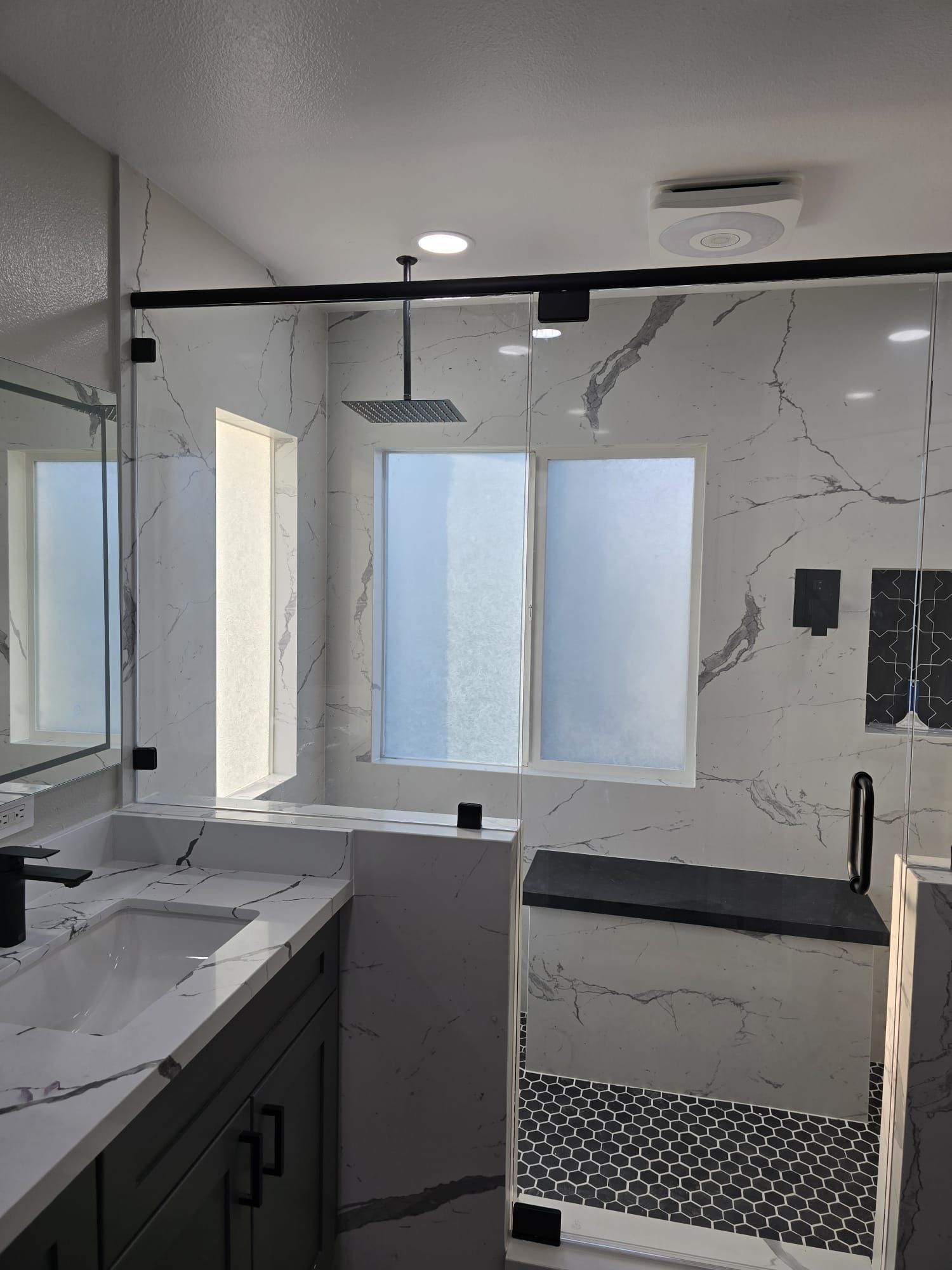 Modern bathroom with a white marble-tiled walk-in shower, black fixtures, and a vanity cabinet.