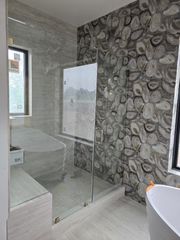 A modern bathroom features a glass-enclosed shower with grey, patterned stone-look wall tiles and a freestanding tub.