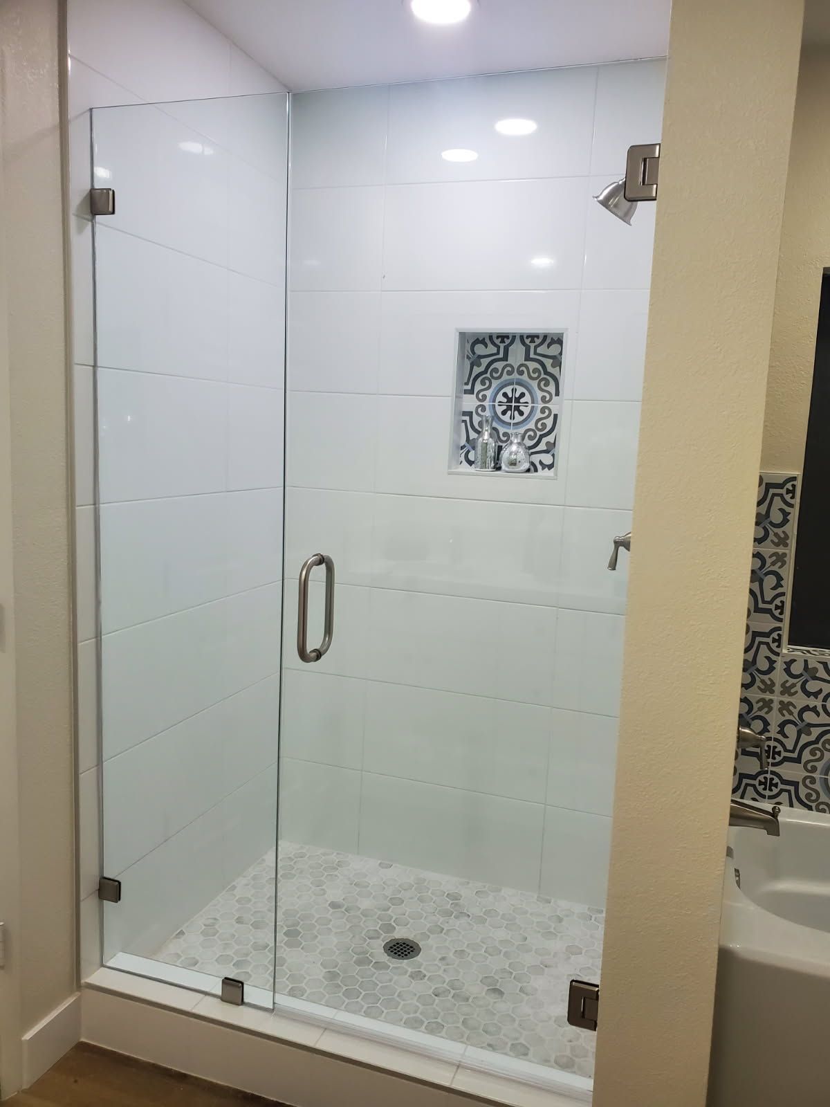 A glass-enclosed shower with white subway tiles, a decorative patterned niche, and a light pebble-style floor.