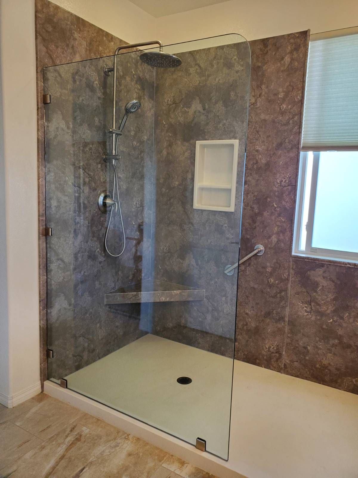 A walk-in shower with stone-look tile walls, a glass panel, a built-in seat, a grab bar, and a rainfall showerhead.