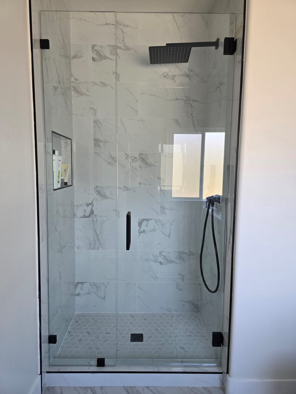 A glass shower enclosure with matte black hardware, featuring marble-style wall tiles and a small storage niche.