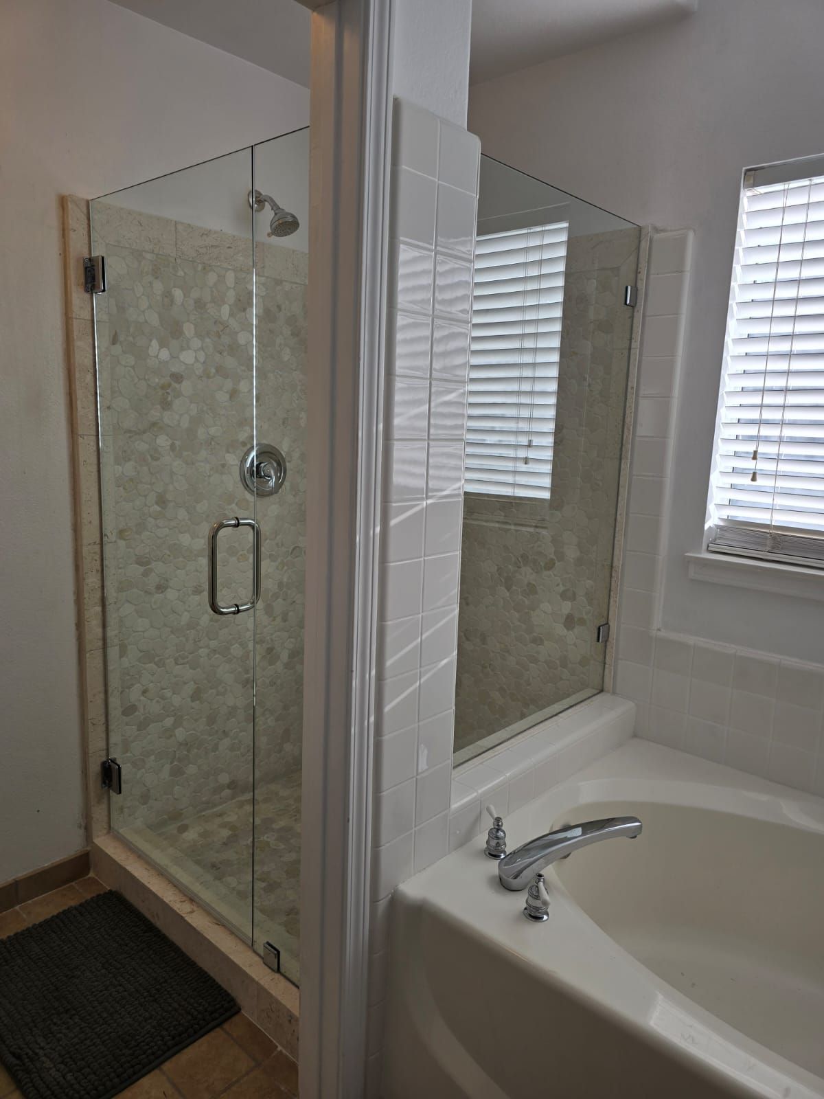 A tiled walk-in shower with a glass door next to a soaking tub in a neutral-toned bathroom.