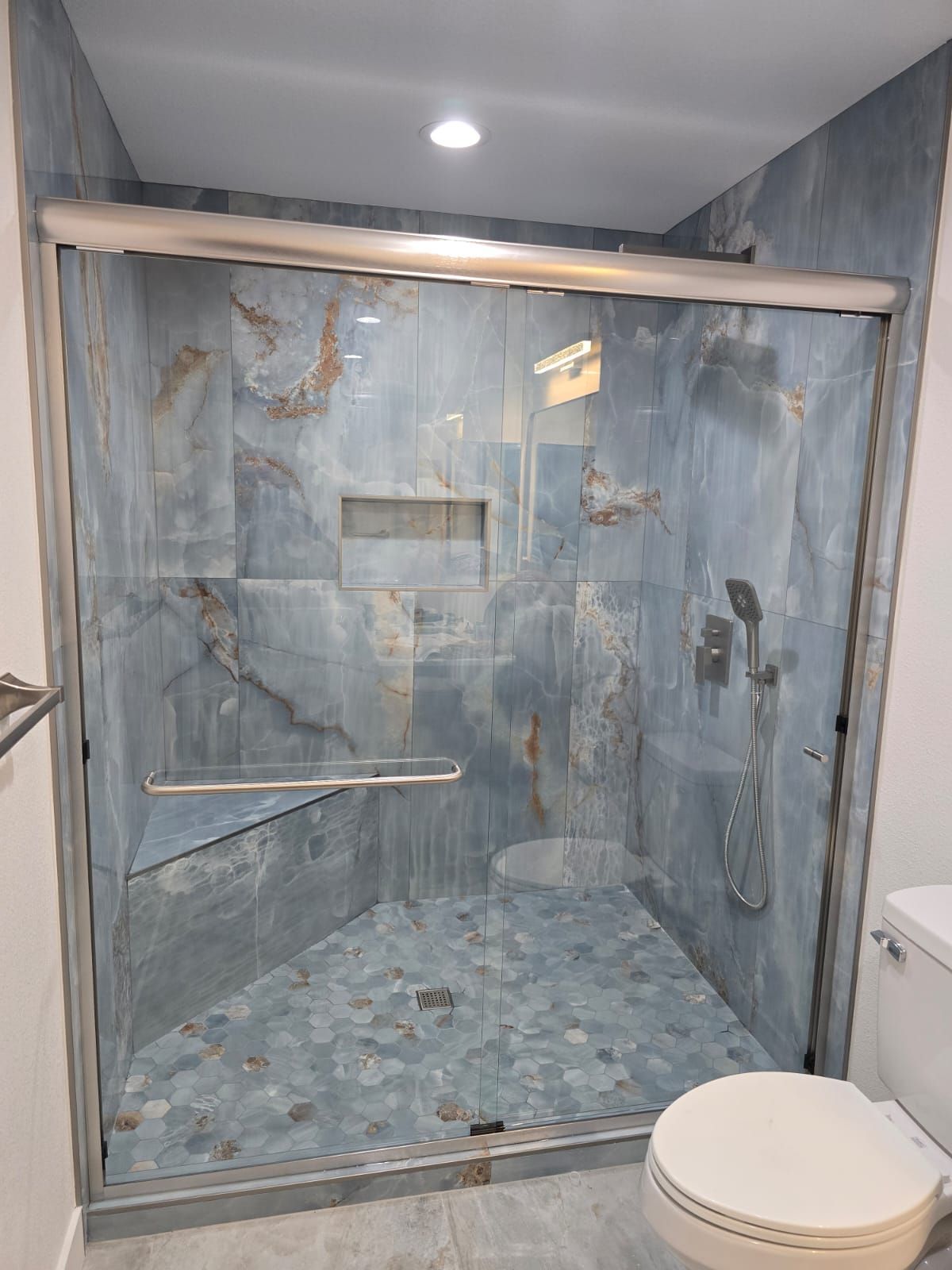 A walk-in shower with blue marble-patterned tiles, a corner bench, a recessed niche, and a glass sliding door.