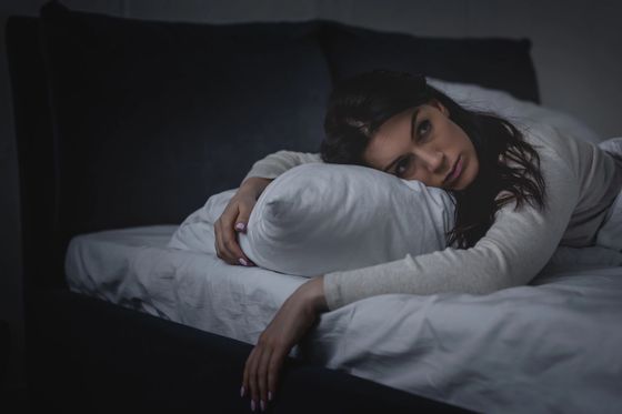 Una donna riposa su un letto, abbracciando un cuscino bianco in una camera da letto scarsamente illuminata.
