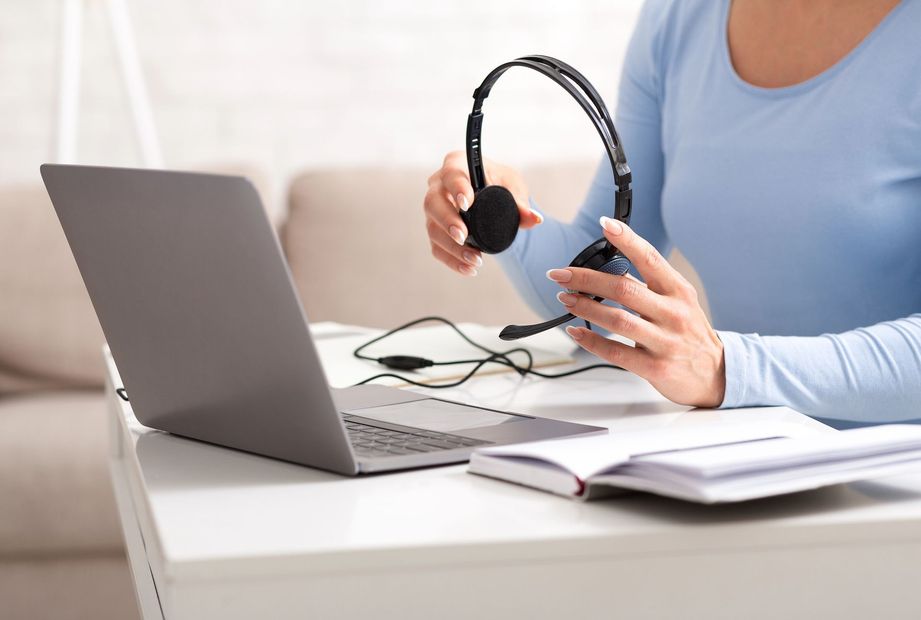 Persona che usa un computer portatile e tiene le cuffie in mano, seduta a una scrivania con un notebook aperto.