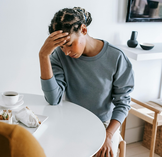 Una persona seduta a un tavolo, con la testa appoggiata su una mano, dall'aria stressata, in un caffè luminoso.