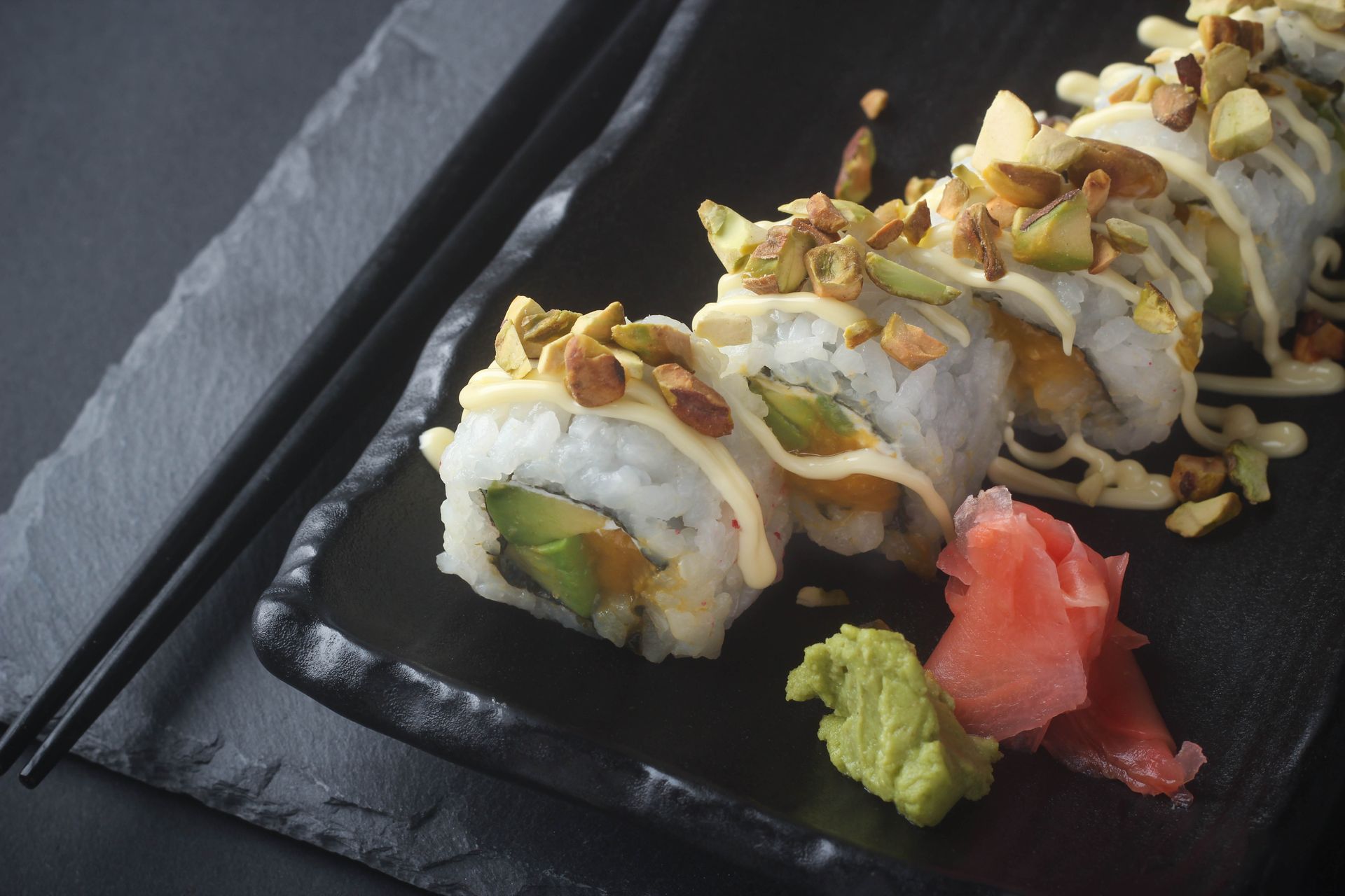 Sushi Restaurant | Finding Sushi | Sushi rolls topped with sliced almonds on a black plate, with wasabi, pickled ginger