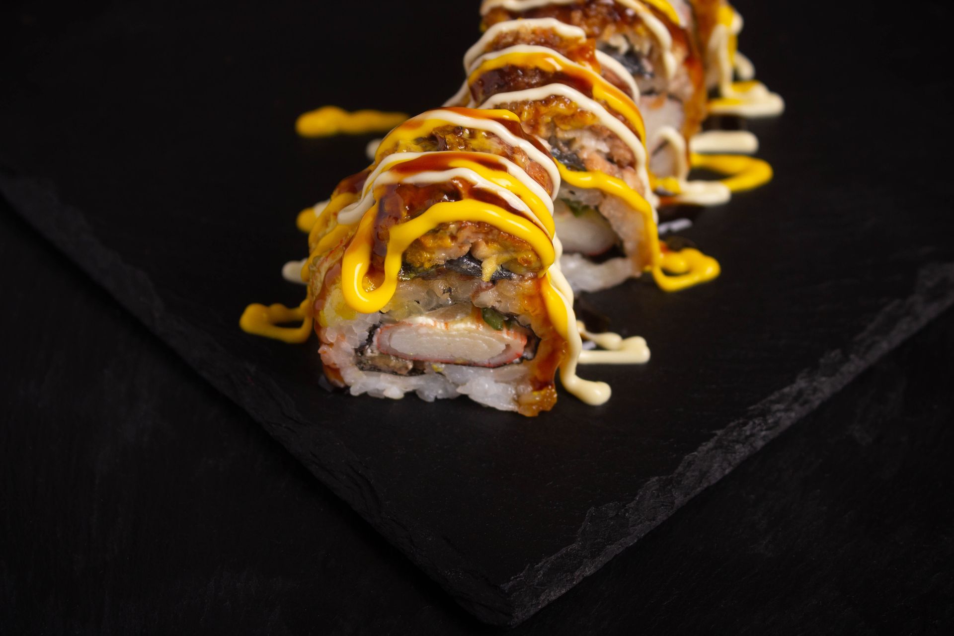 Sushi Restaurant | Finding Sushi | Sushi rolls drizzled with orange and white sauce on a black slate board