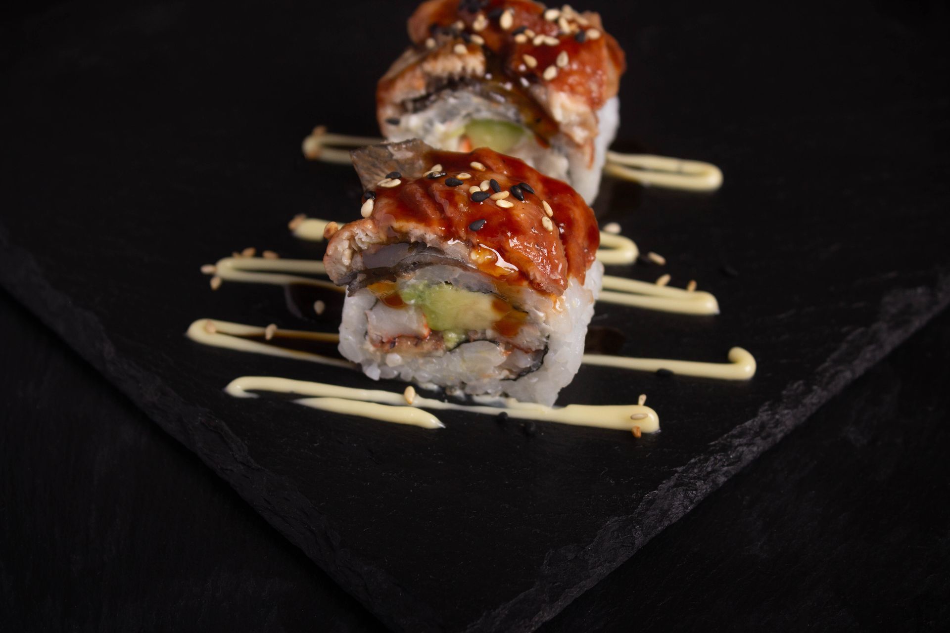 Sushi Restaurant | Finding Sushi | Sushi rolls drizzled with sauce on a dark slate plate