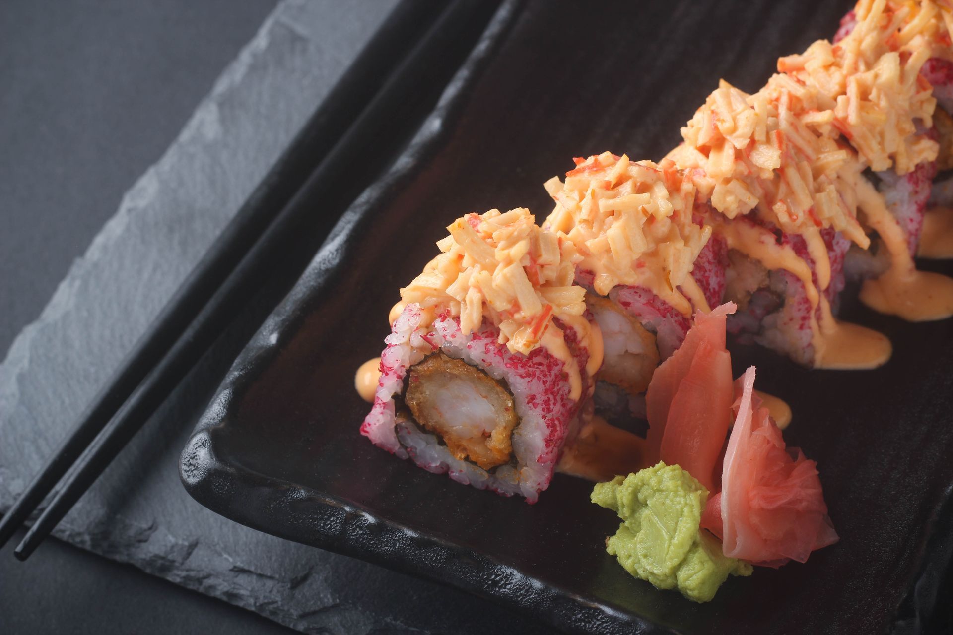 Sushi Restaurant | Finding Sushi | Sushi rolls topped with crispy bits on a black plate, with wasabi and pickled ginger