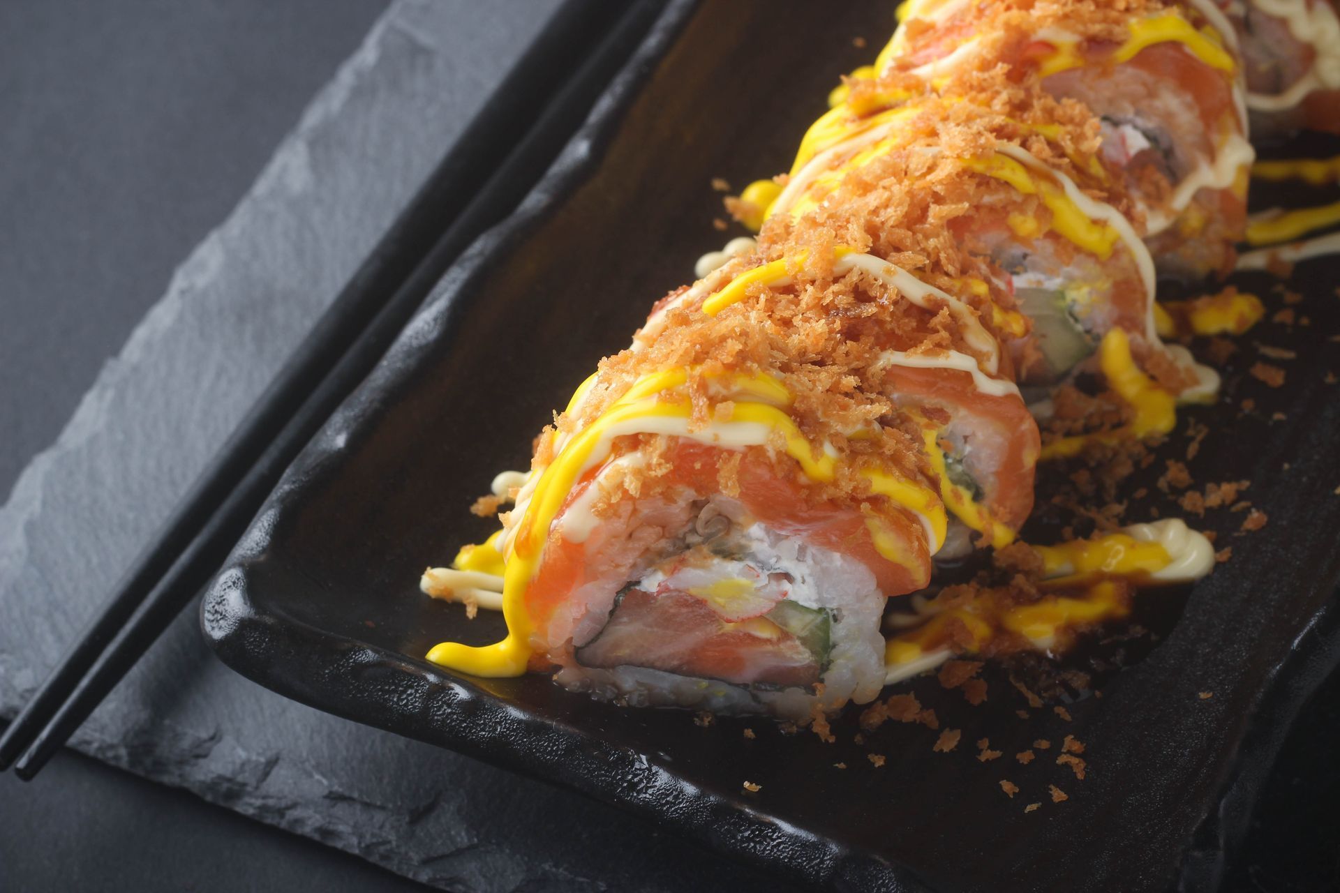 Sushi Restaurant | Finding Sushi | Sushi rolls drizzled with sauce on a black rectangular plate with chopsticks