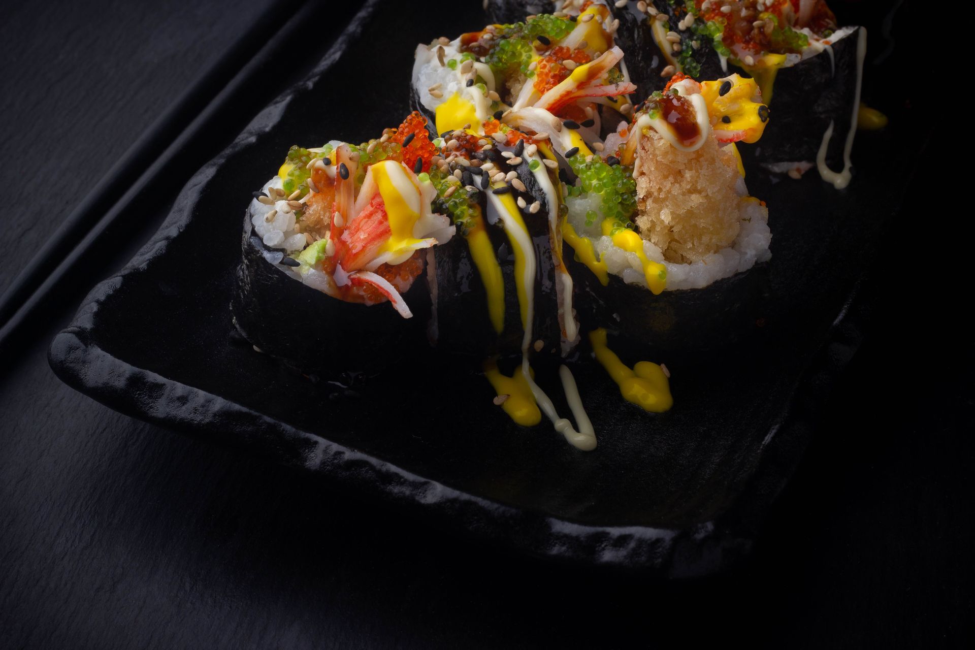 Sushi Restaurant | Finding Sushi | Sushi rolls topped with colorful vegetables and sauces on a black square plate