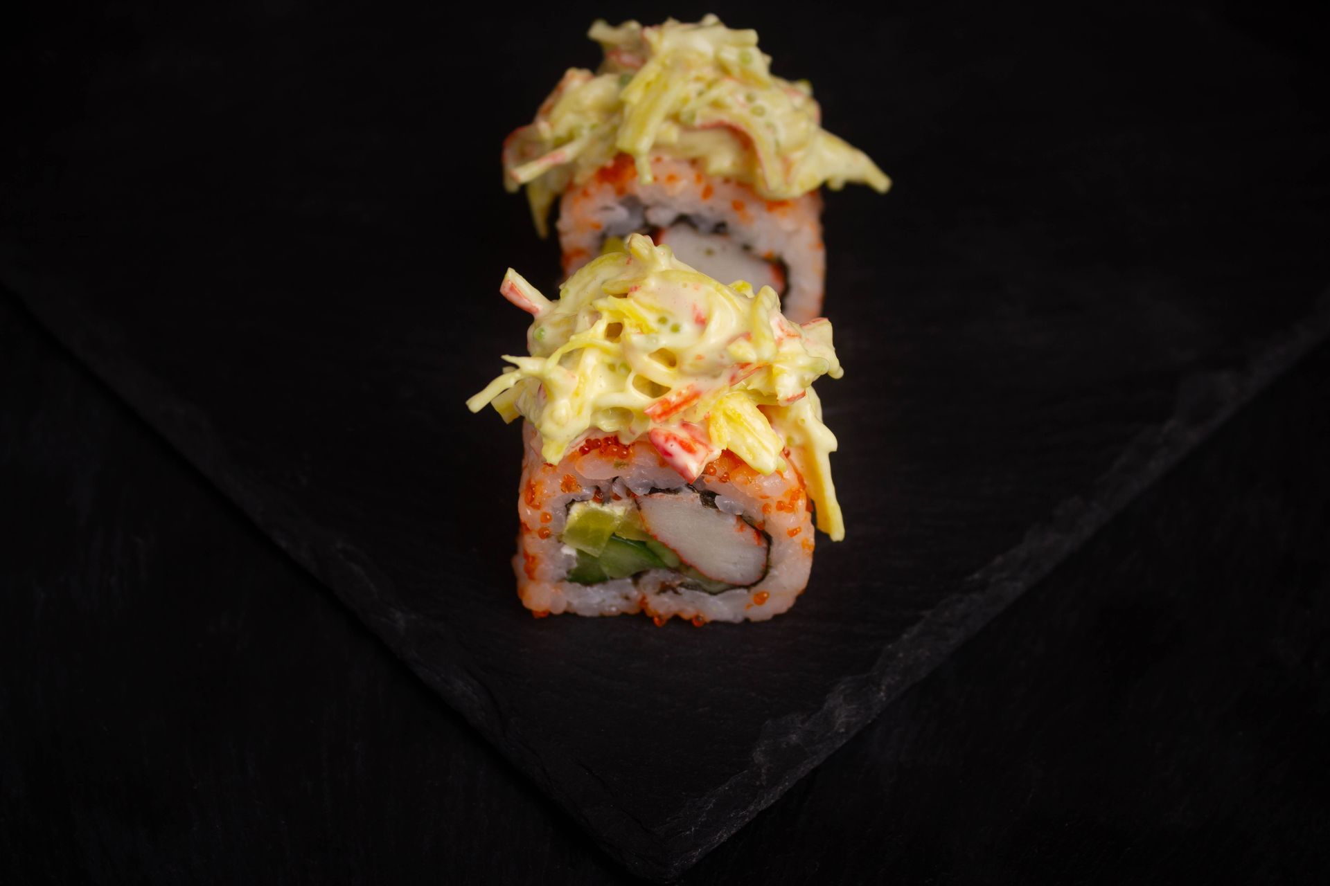 Sushi Restaurant | Finding Sushi | Sushi roll topped with shredded cheese, cut into pieces on a dark plate.