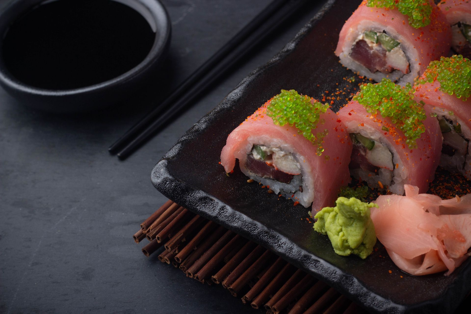 Sushi Restaurant | Finding Sushi | Sushi rolls topped with green garnish on a black plate, with wasabi, pickled ginger,
