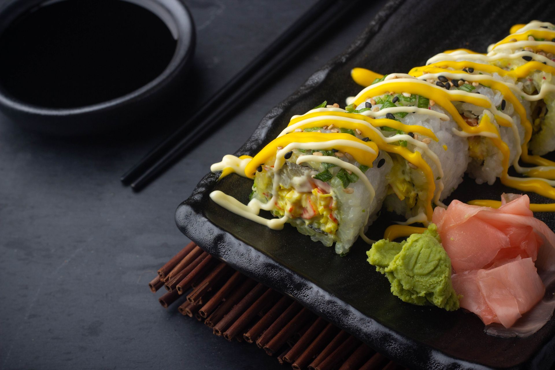 Sushi Restaurant | Finding Sushi | Sushi rolls drizzled with sauce, with pickled ginger, wasabi, and chopsticks.