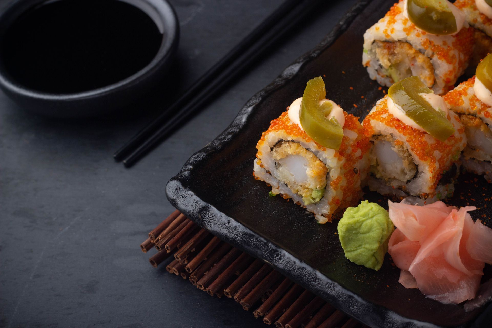 Sushi Restaurant | Finding Sushi | Sushi rolls on a black plate with soy sauce, chopsticks, wasabi, and pickled ginger