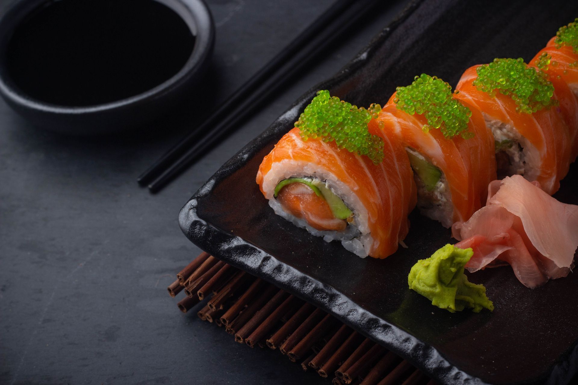 Sushi Restaurant | Finding Sushi | Salmon sushi rolls with green garnish, with chopsticks and soy sauce nearby