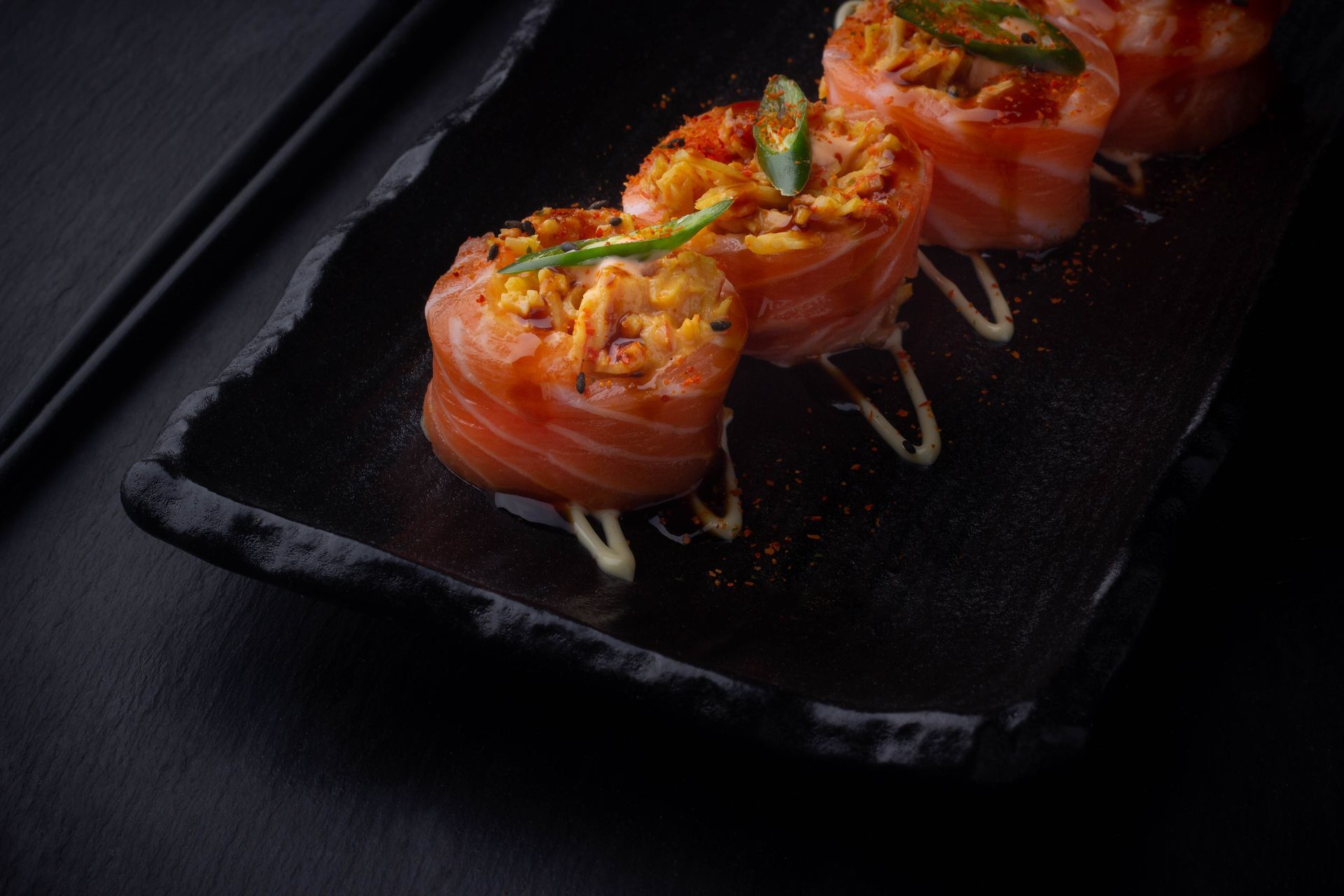 Sushi Restaurant | Finding Sushi | Sushi rolls topped with salmon, garnished with herbs and sauce.