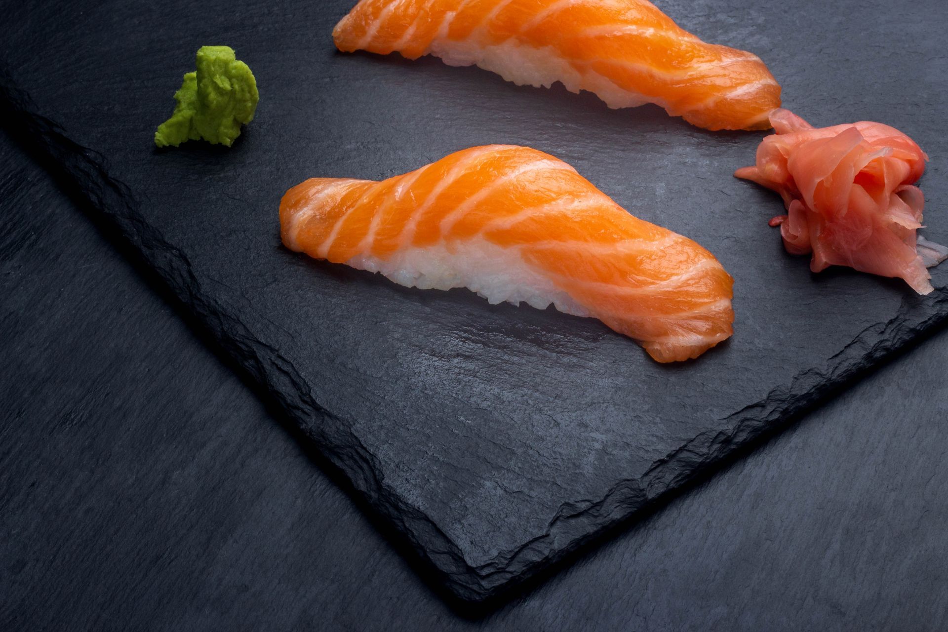 Sushi Restaurant | Finding Sushi | Two slices of salmon sushi on a black slate plate with wasabi and pickled ginger