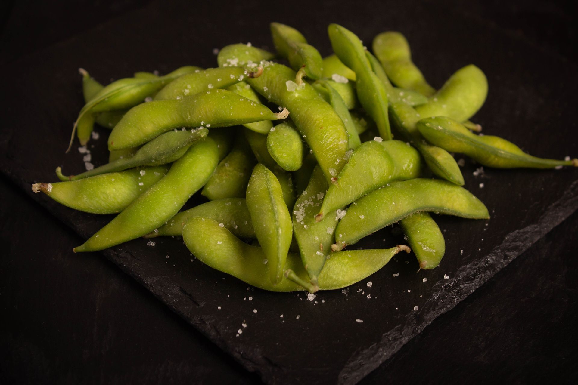 Sushi Restaurant | Finding Sushi | Green edamame pods piled on a dark serving plate with coarse salt