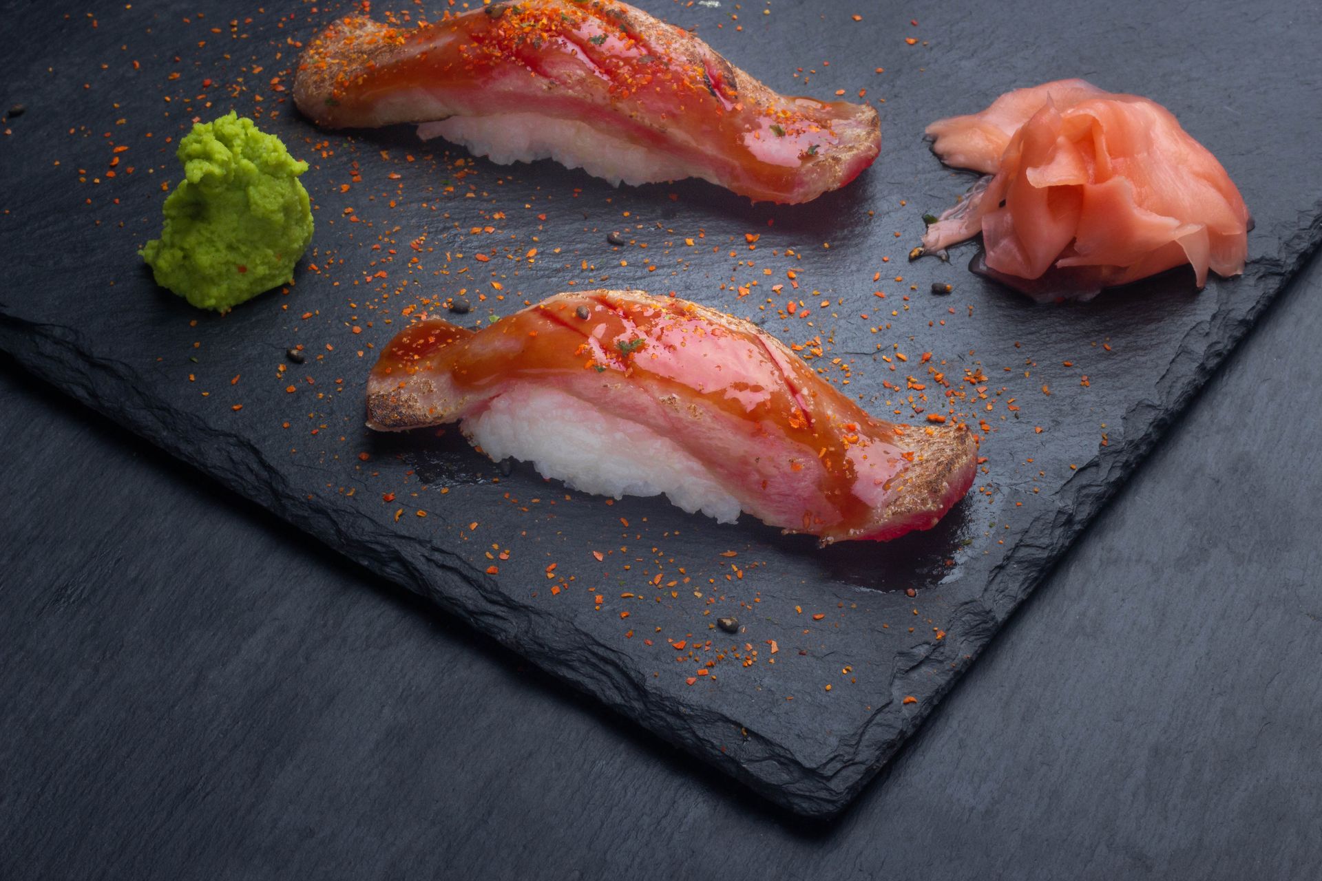Sushi Restaurant | Finding Sushi | Two pieces of glazed sushi on a black slate plate with wasabi and pickled ginger