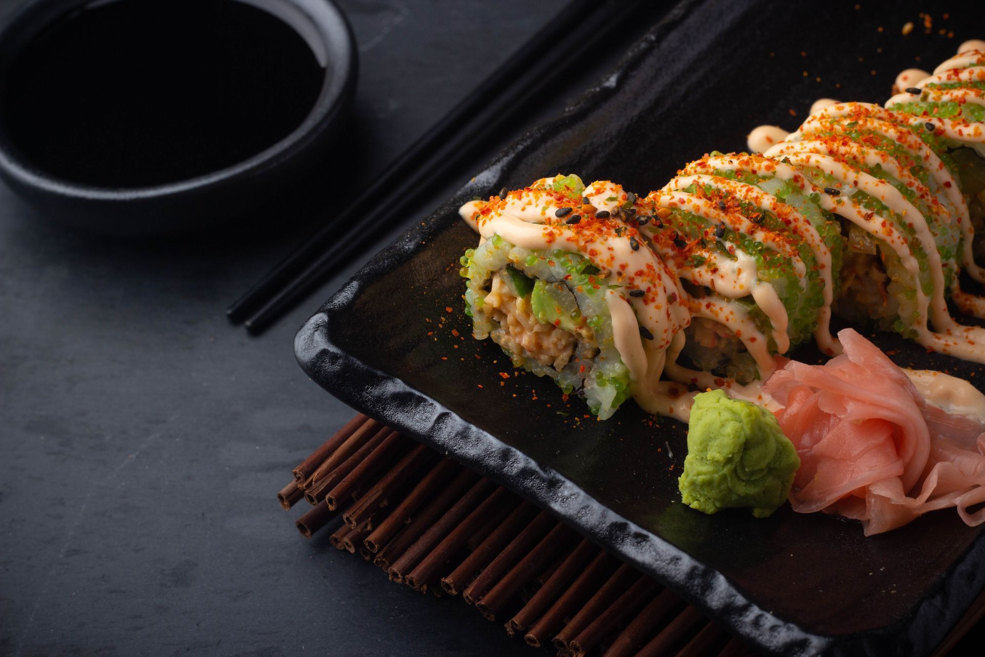 Sushi Restaurant | Finding Sushi | Sushi rolls on a black plate with green wasabi and pink ginger on a dark table