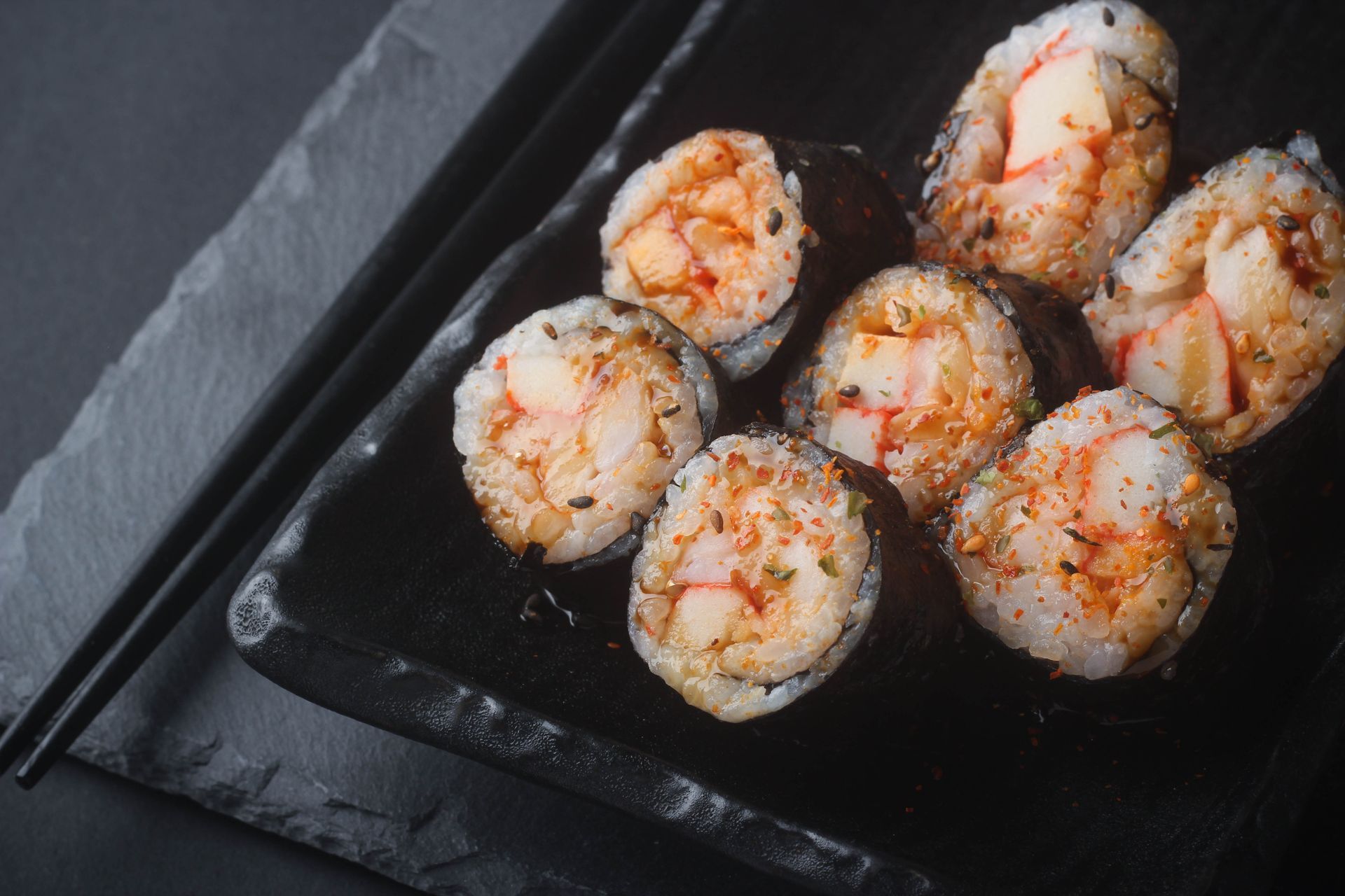 Sushi Restaurant | Finding Sushi | Rice balls sprinkled with red seasoning on a black plate beside chopsticks