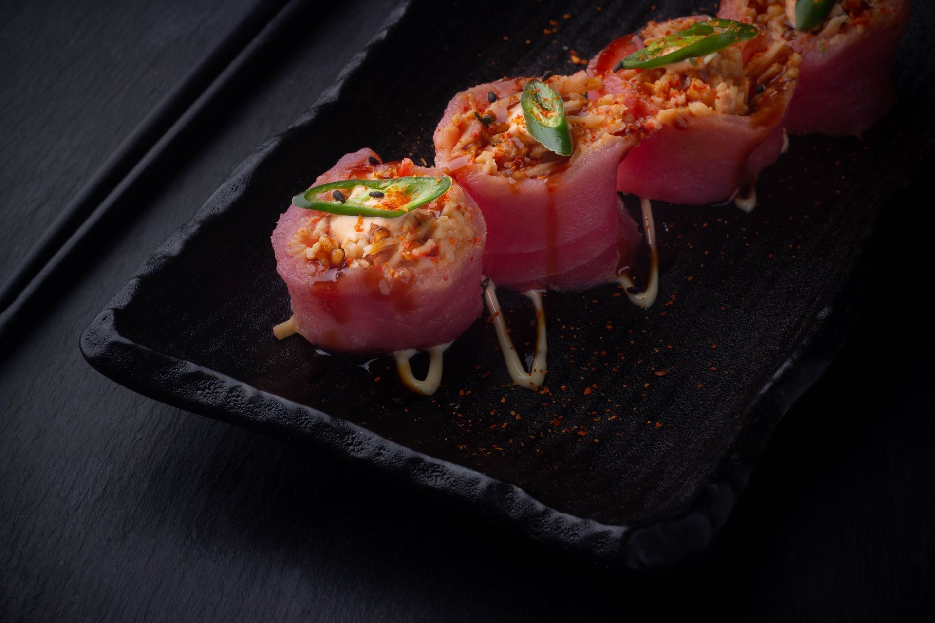 Sushi Restaurant | Finding Sushi | Sushi rolls topped with spicy salmon and herbs on a black rectangular plate