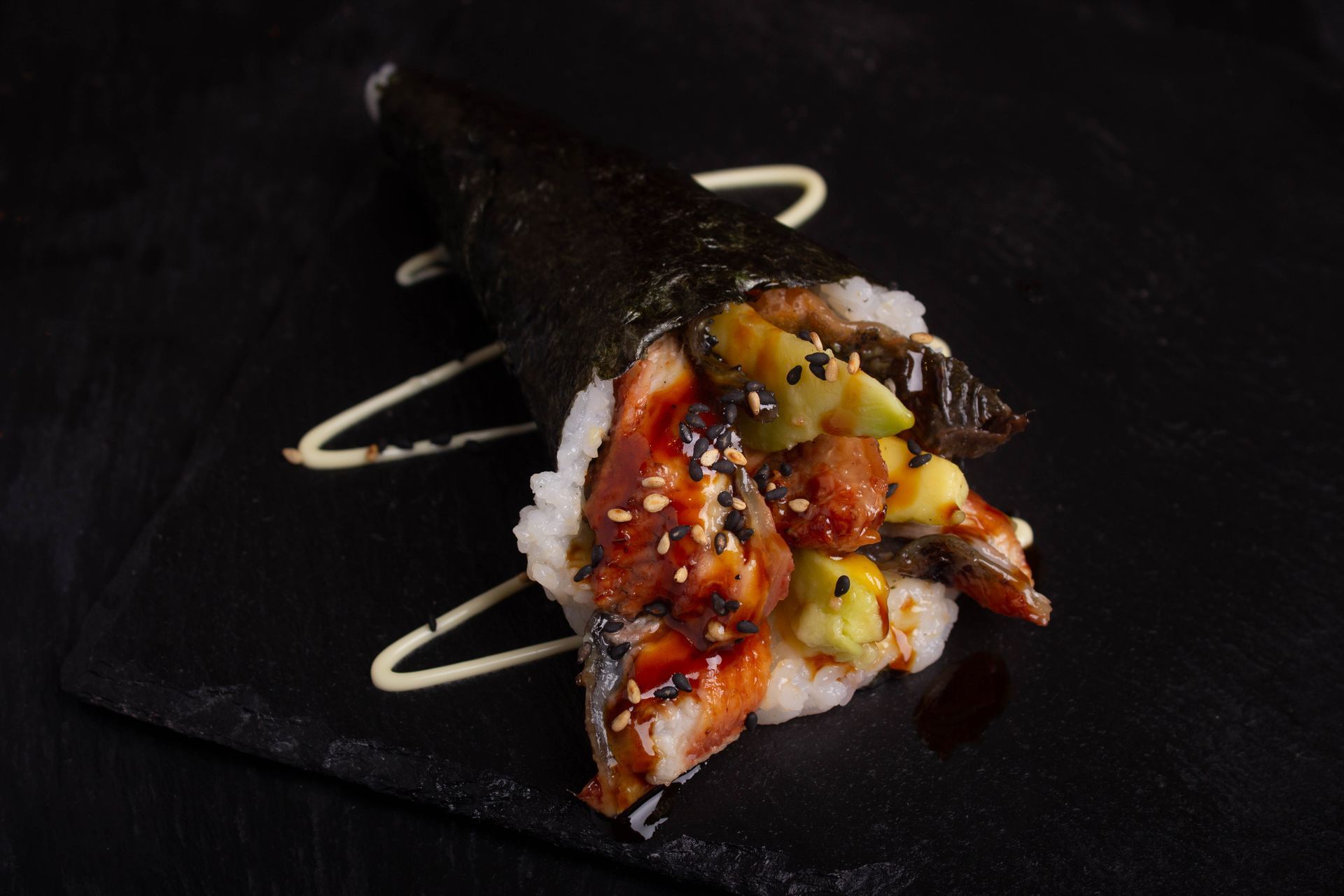 Sushi Restaurant | Finding Sushi | Sushi hand roll with white rice, glazed fish, and green garnish on a dark plate