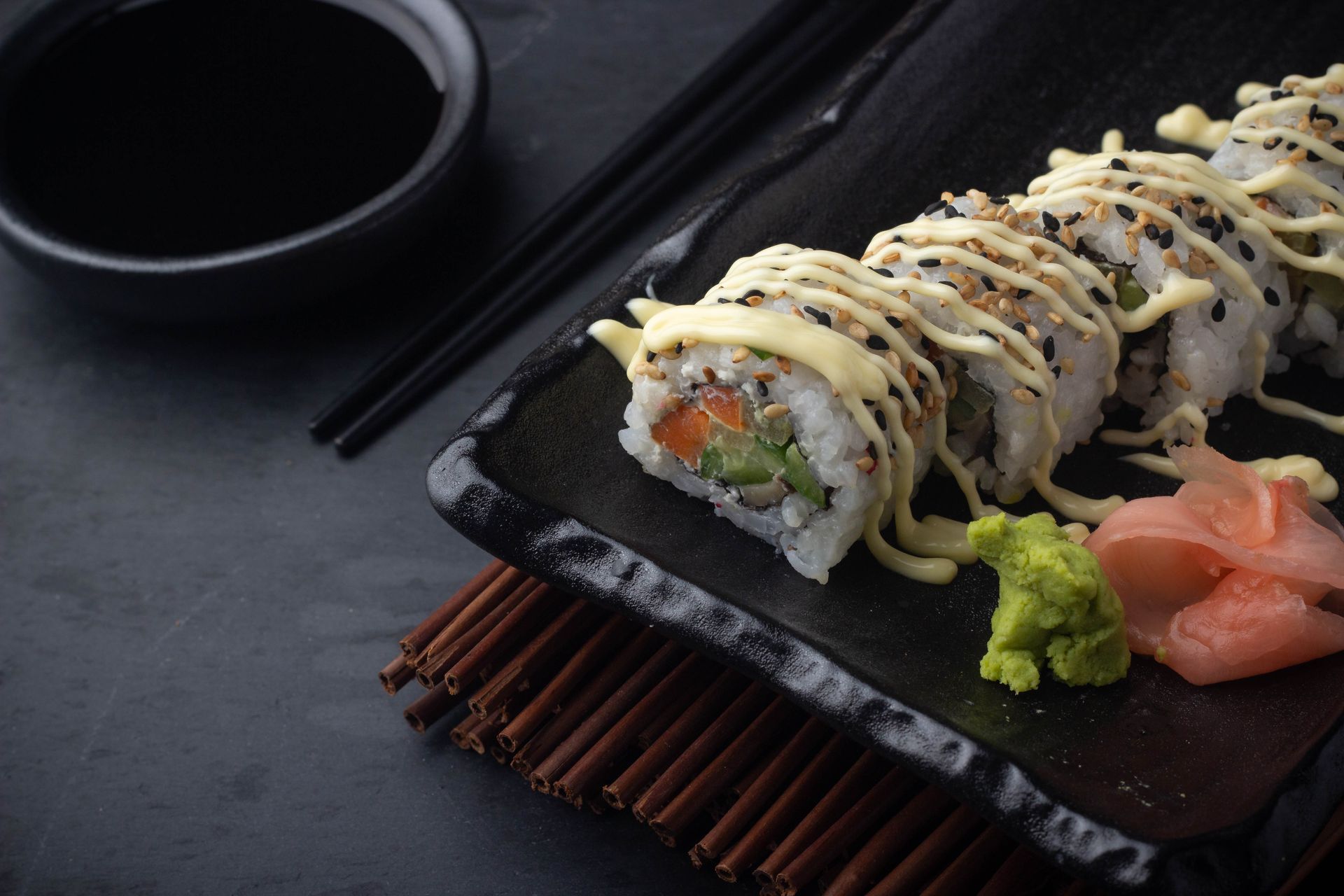 Sushi Restaurant | Finding Sushi | Sushi rolls on a black plate with chopsticks, wasabi, and pickled ginger on a dark table