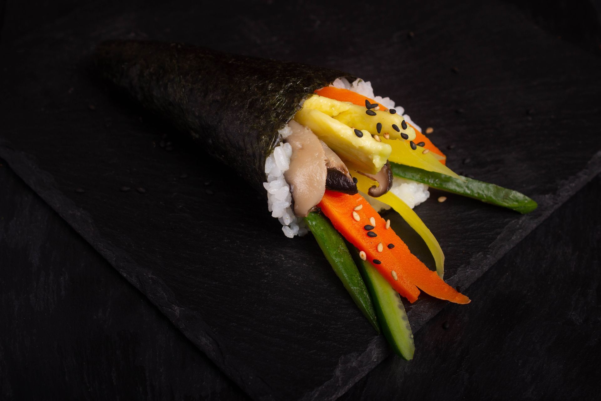 Sushi Restaurant | Finding Sushi |Sushi roll with rice, avocado, salmon, yellow fruit, and black sesame on a dark plate