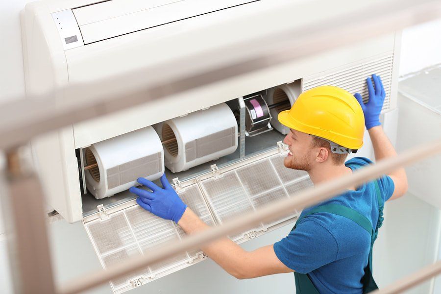 A man wearing a hard hat and gloves is working on an air conditioner.