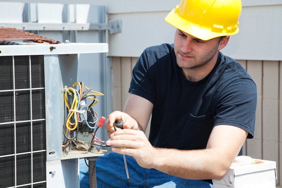 A man wearing a hard hat is working on an air conditioner.