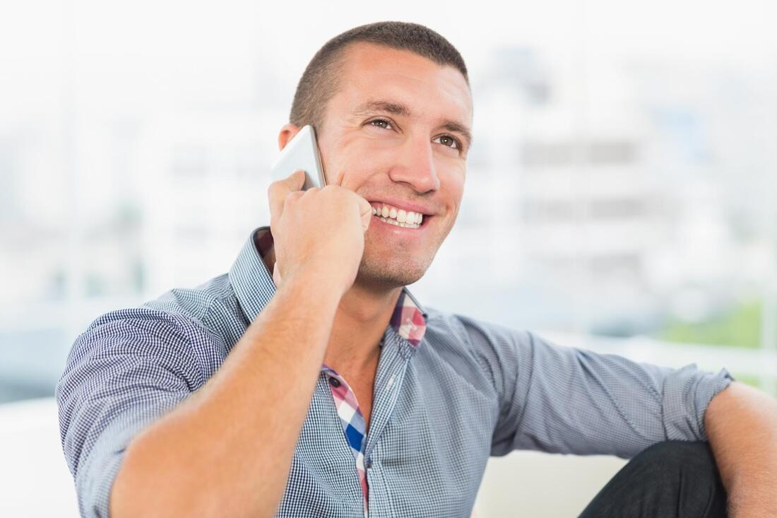 A man is sitting on a couch talking on a cell phone.